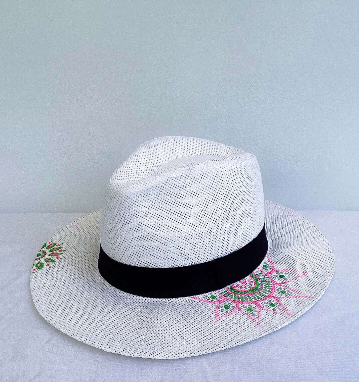 Panama hat, black band at base, with hand painted green and pink mandalas asymmetrically positioned.