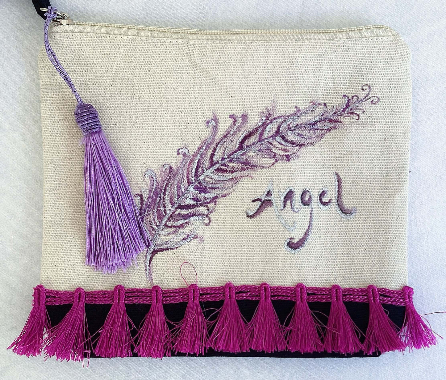 Front of canvas pouch, black canvas base, with hand painted feather, magenta trim at the base, lavender tassel and zip.