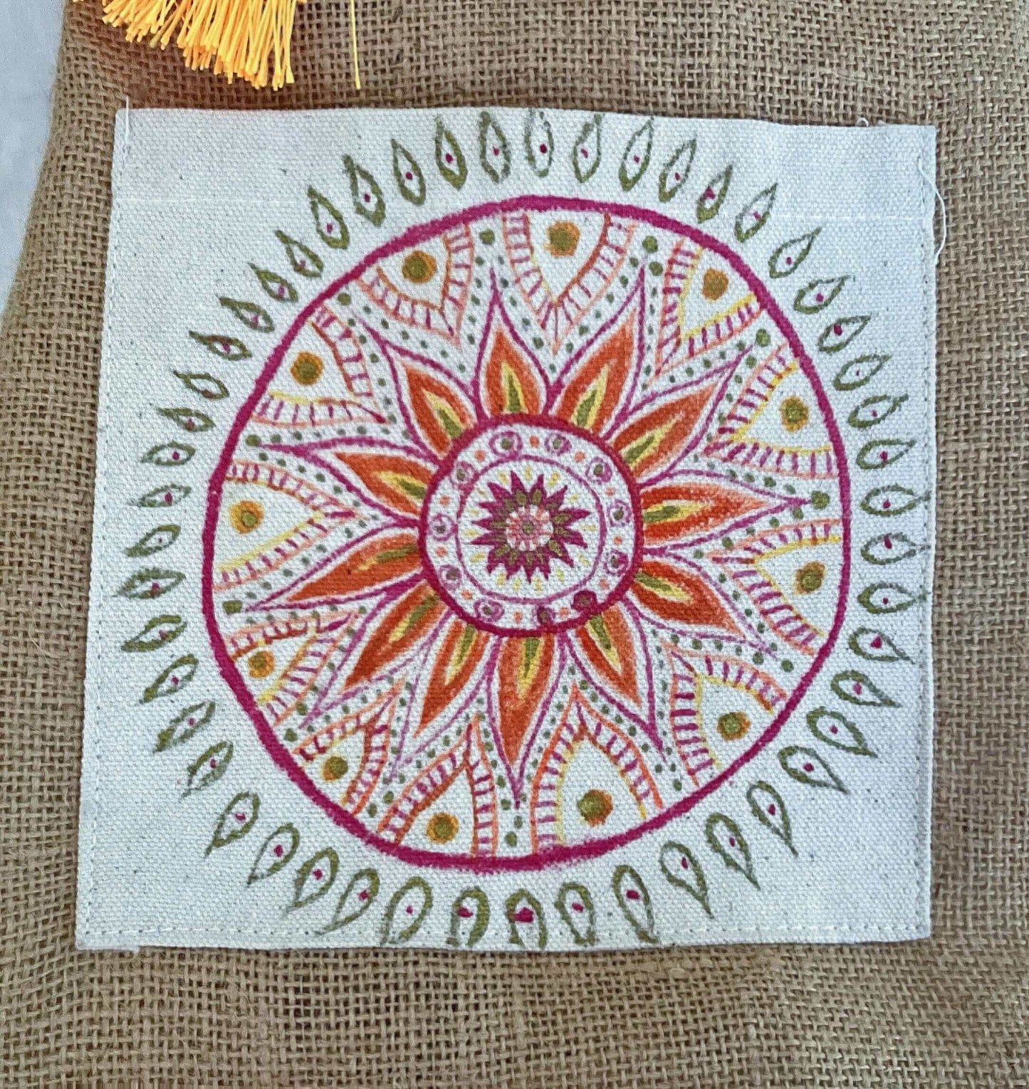 Close up view of hessian satchel with hand painted red, orange, gold mandala on canvas patch.