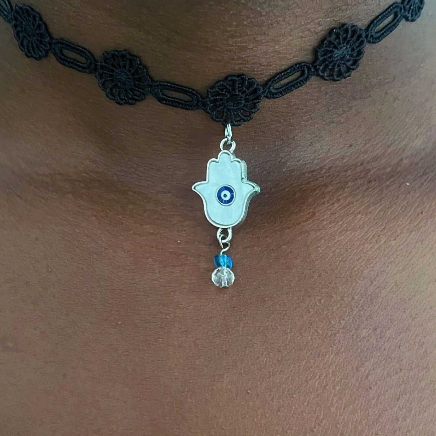 Detail view of enamel and beaded hamsa on embroidered black choker.