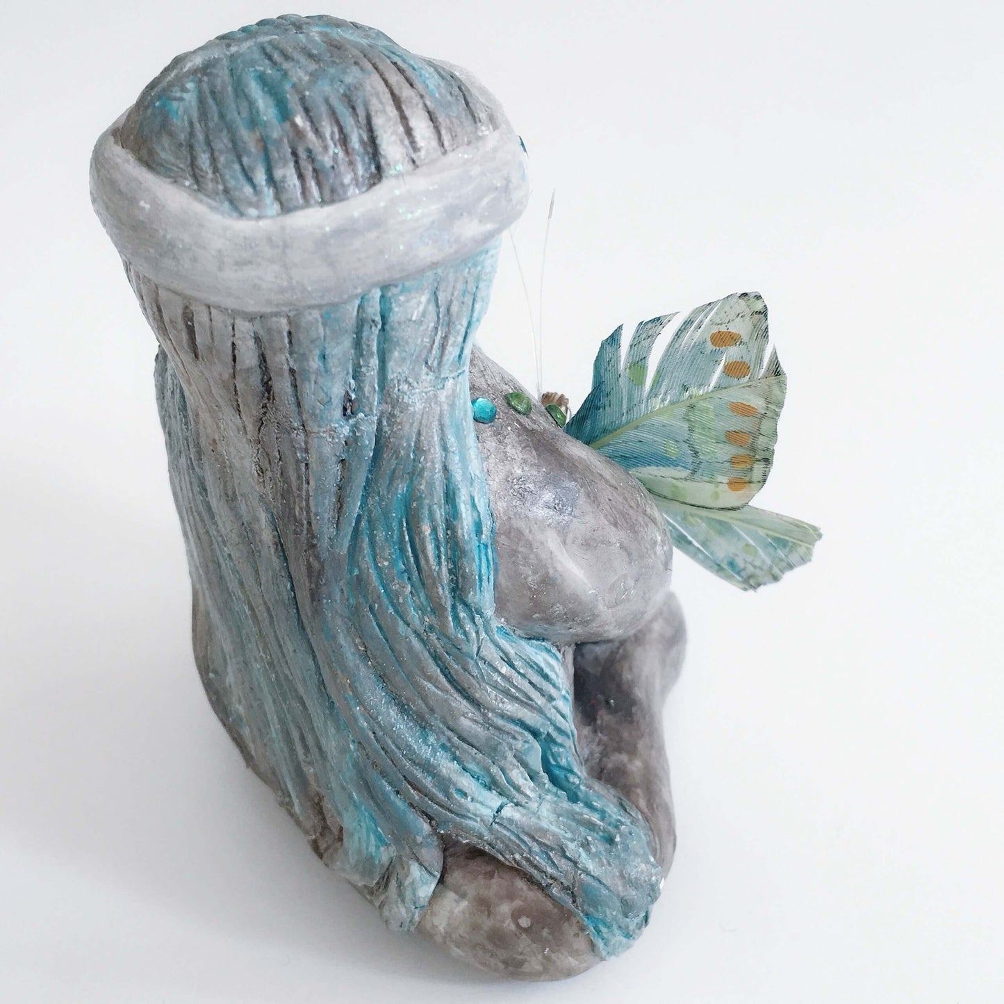 Back of elemental, brown wash painted figure, jewel band on head, bluish long hair, holding a feather butterfly.