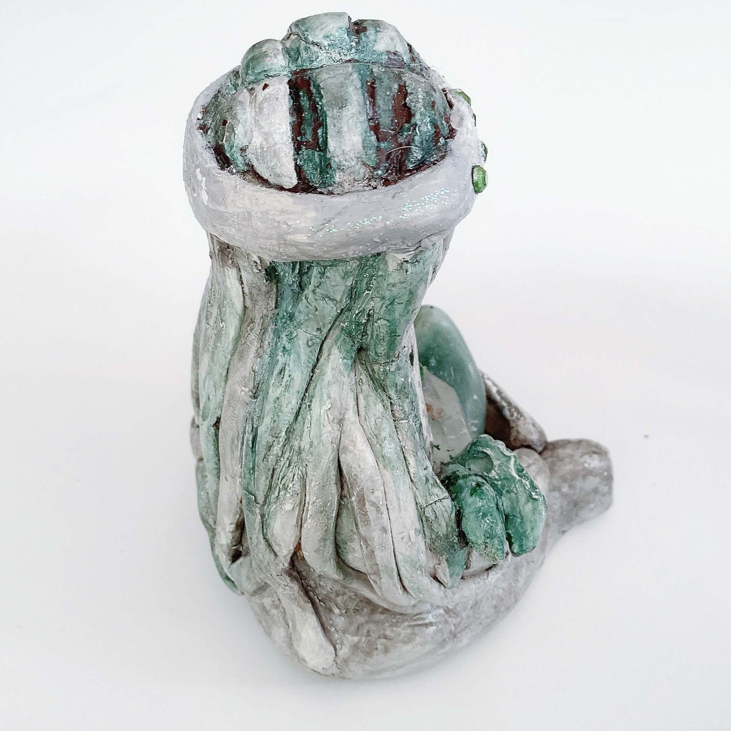 Back of elemental, brown wash painted figure, jewel band on head, pale green long hair, holding crystals and clay leaves.