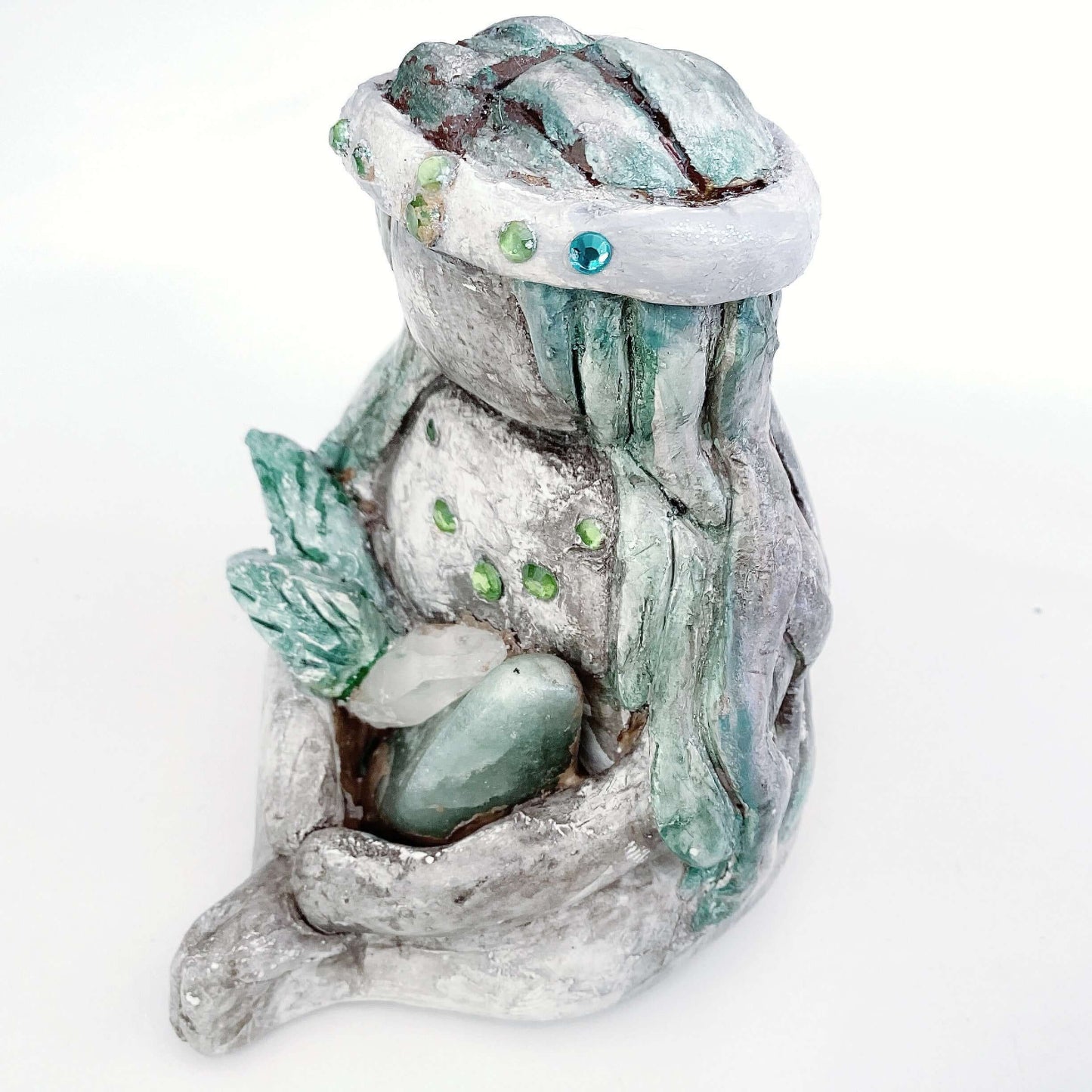 Left of elemental, brown wash painted figure, jewel band on head, pale green long hair, holding crystals and clay leaves.