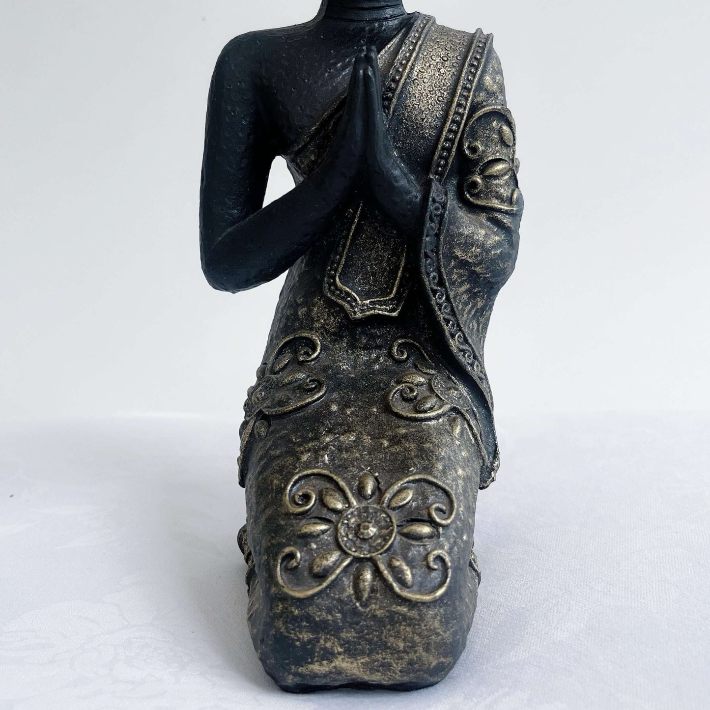 Detail view of buddha kneeling, with ornate robes and detailing, washed black and silver painting