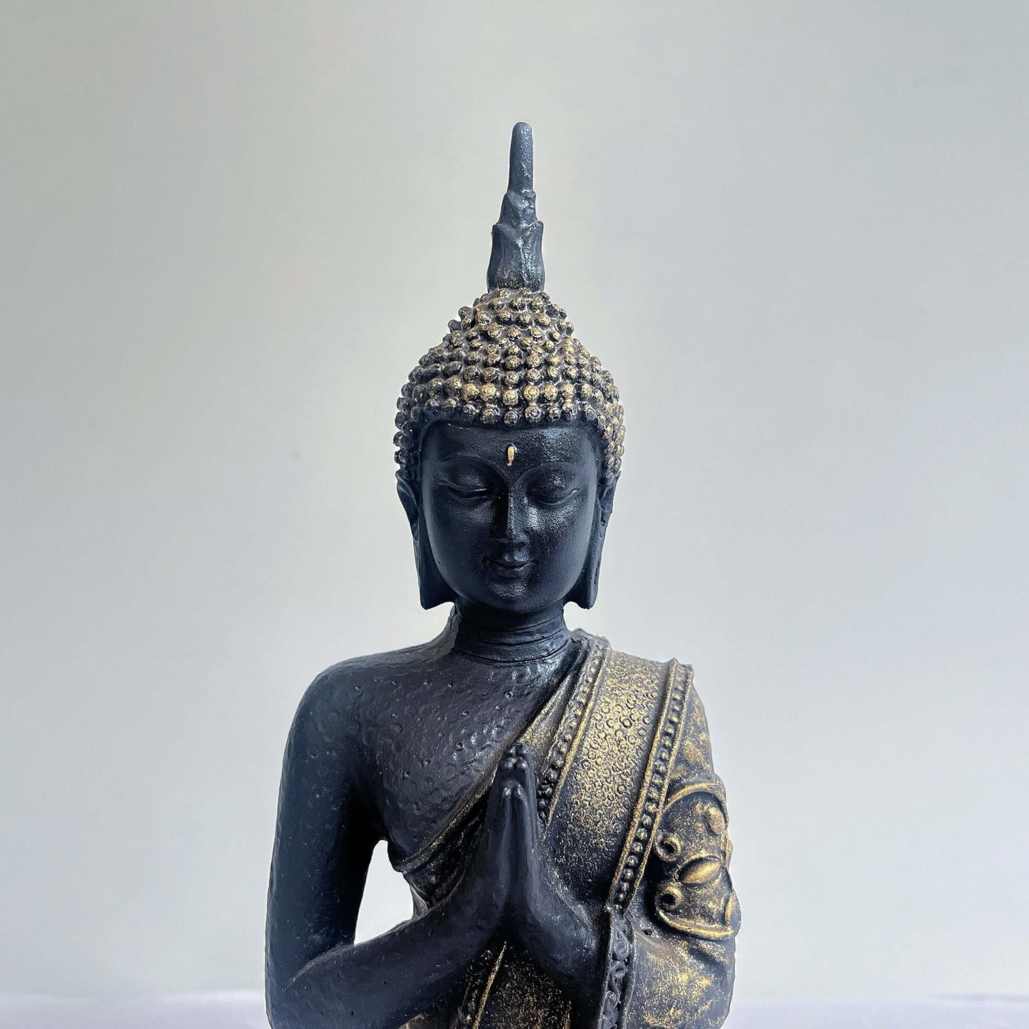 Detail view of buddha torso, with ornate robes and detailing, ushnisha on head, washed black and silver painting.