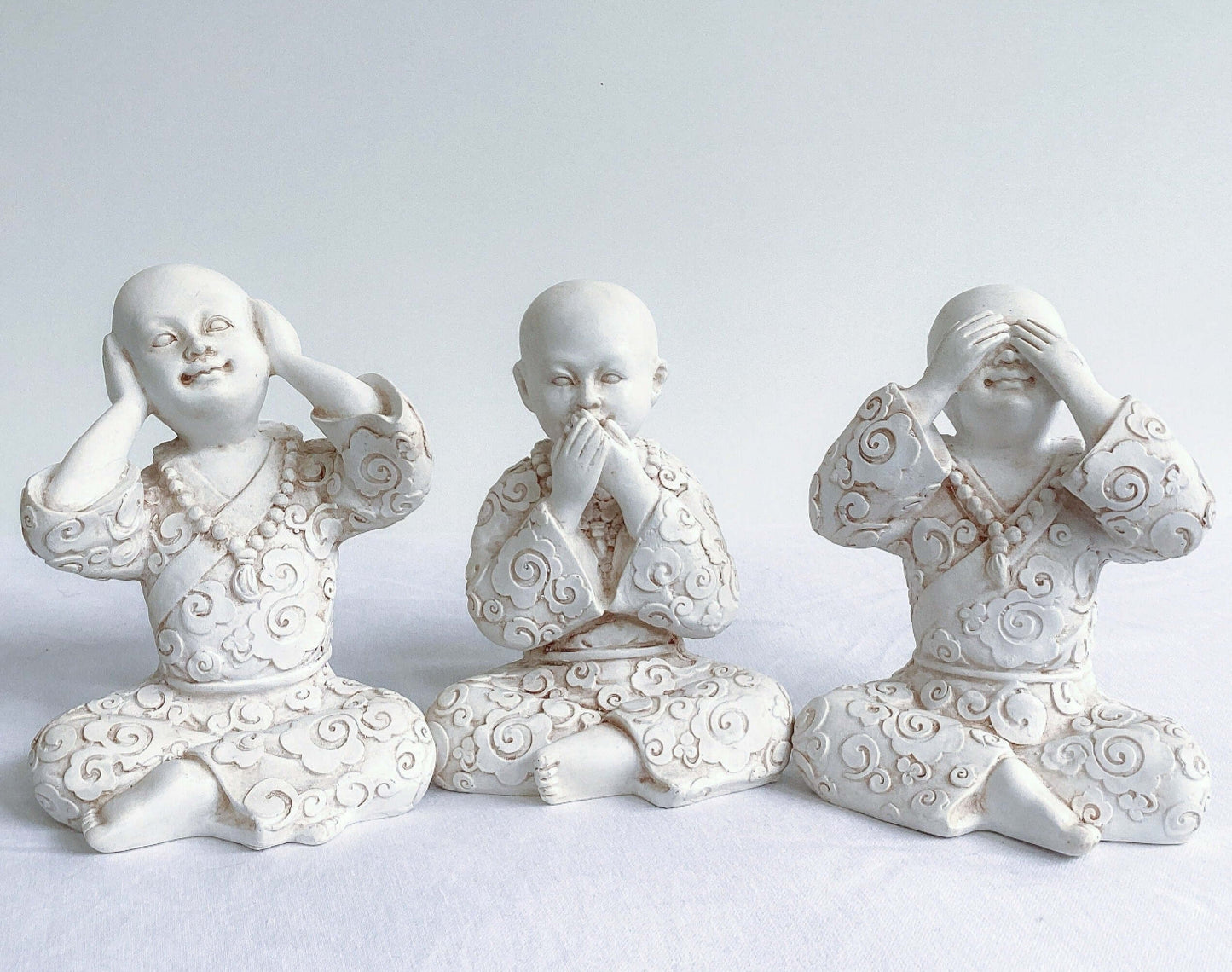 Front view of monks, all three in a row, natural off white colors, with ornate robes.