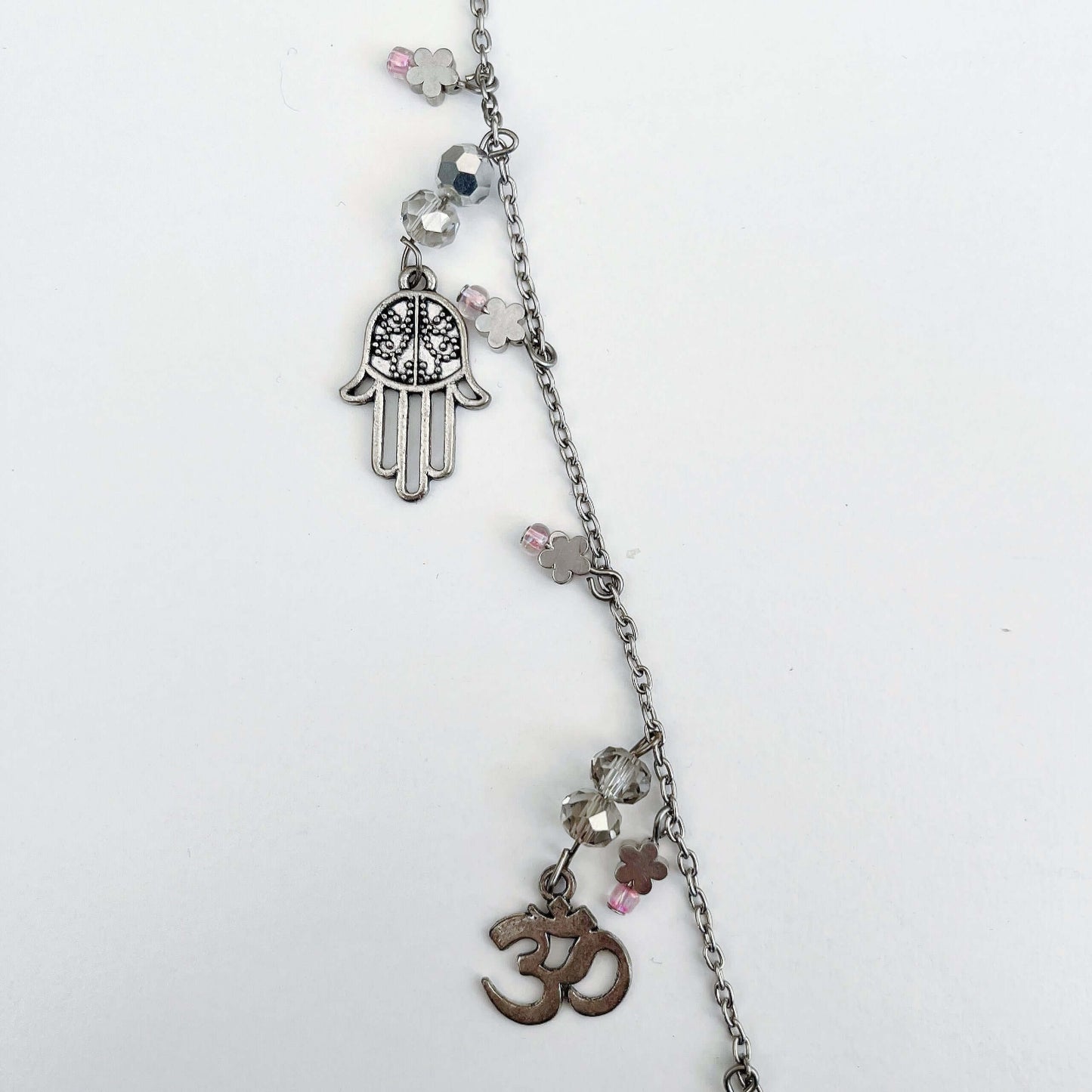 Detail view of charm necklace, showing hamsa hand and om sign.