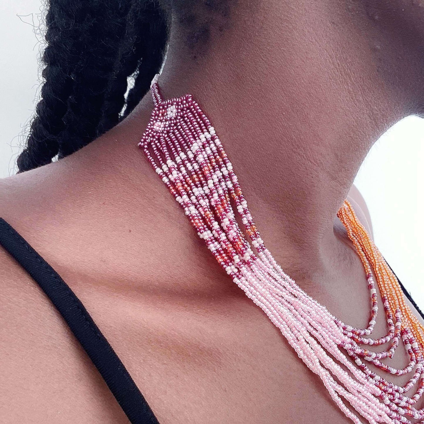 Detail view of thirteen strand zulu beaded necklace, in bands of pink and orange, alternating with multi color beads.