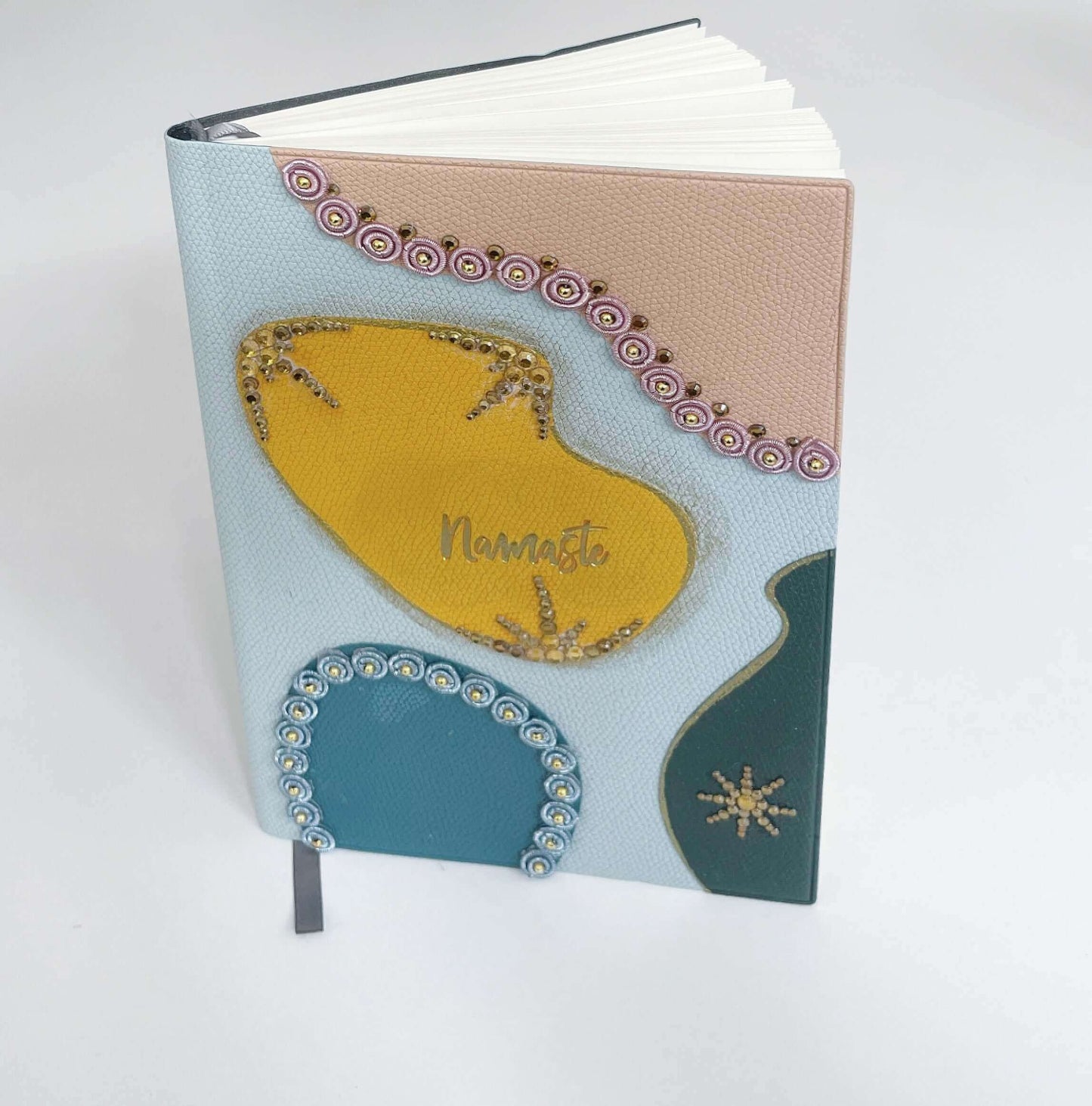 View of journal upright, showing blotches of color in yellow, peach, blue, black, with crystal deco on their borders.