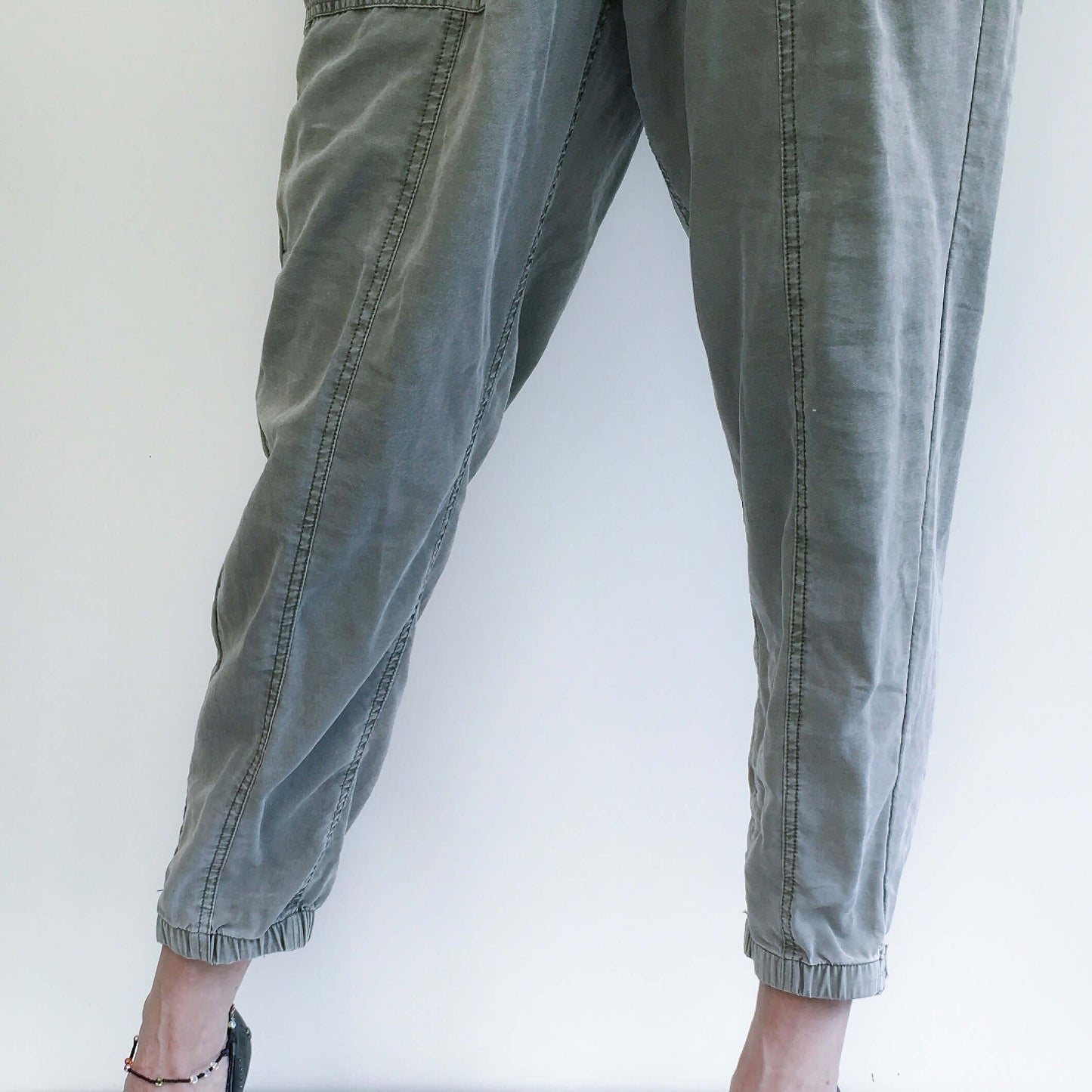 Detail view of pale khaki elasticated pants with belt, side pockets, and elasticated ankles.