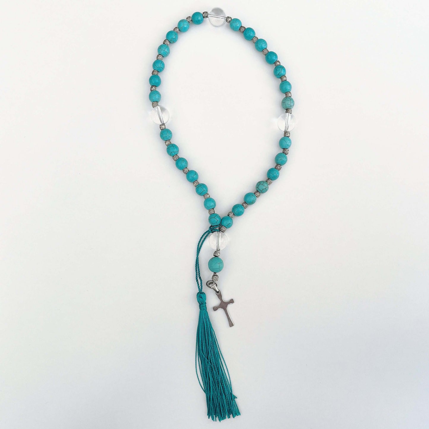 Top view of prayer beads, Blue Howlite sections, with one clear quartz here and there. Cross and tassel at the bottom.