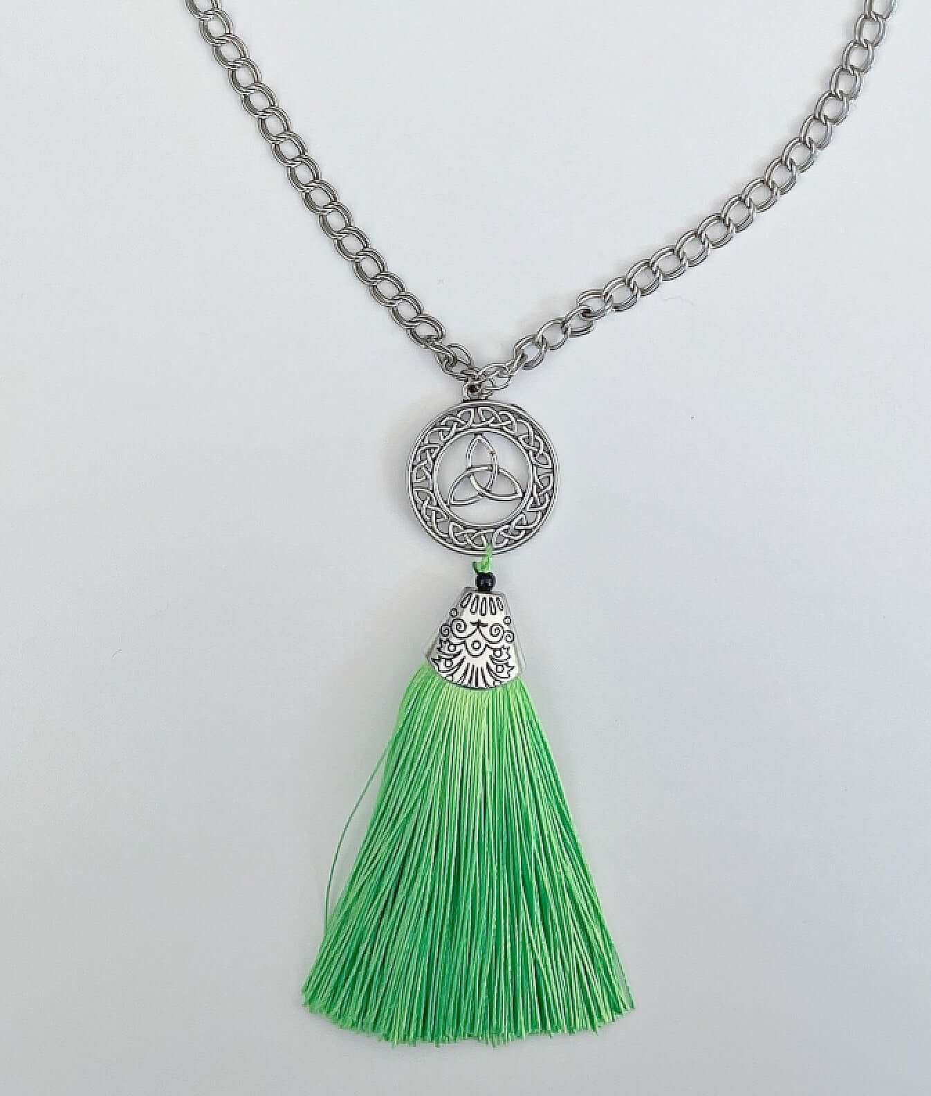 Detail view of necklace with green tassel off the end, which has a silver finish filigree cap on it, round link chain.