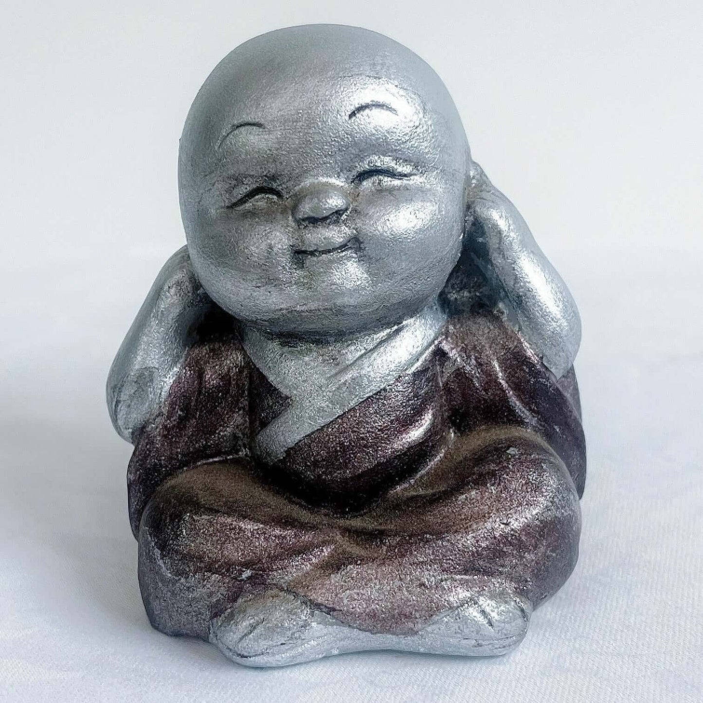 View of single monk, hear no evil, painted silver figure with bronze robes, and hands covering the ears.