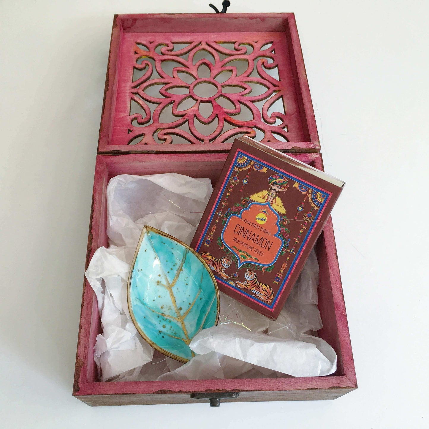 Contents detail view of incense and turquoise painted ceramic leaf, nestled in white tissue paper and tinsel.