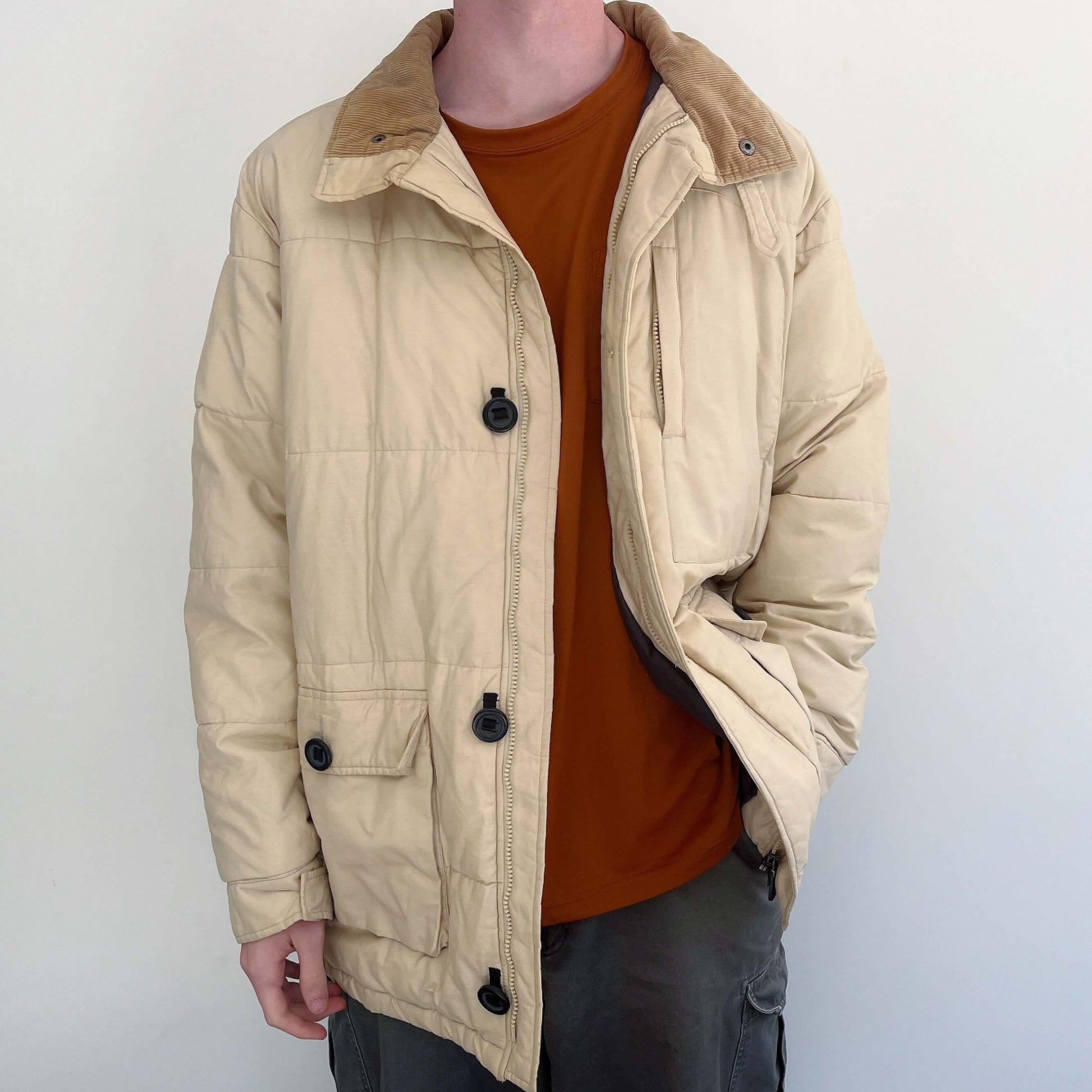 Front view of the beige padded jacket, with two button down side pockets, shown unzipped, with 4 large black buttons.