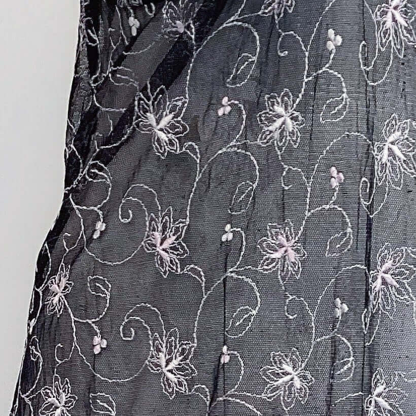 Detail view of black net fabric, with very pale pink floral embroidery. Mid thigh length.