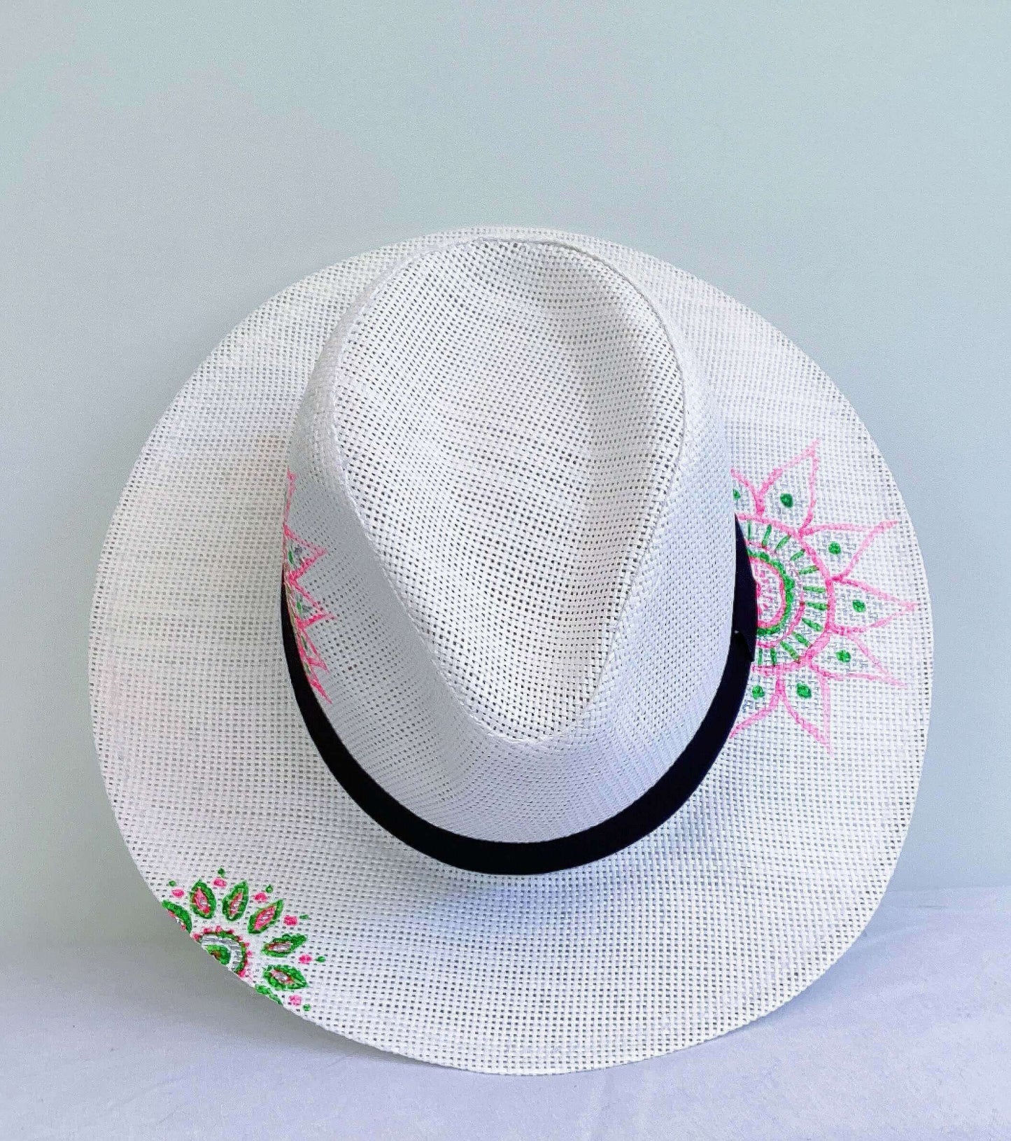 Aerial view of panama hat, black band at base, with hand painted green and pink mandalas asymmetrically positioned.