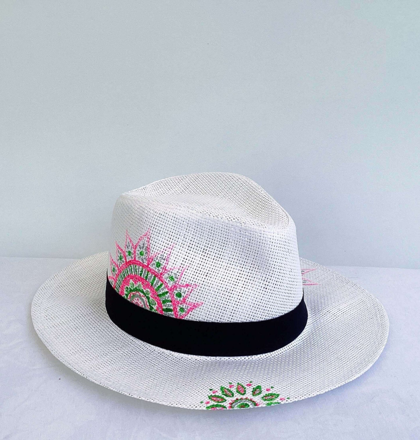 Side view of panama hat, black band at base, with hand painted green and pink mandalas asymmetrically positioned.