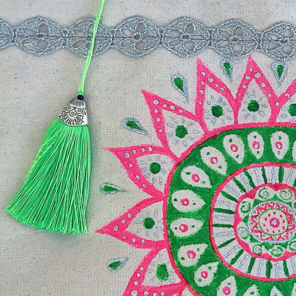 Close up view of canvas tote bag, with large hand painted green and pink mandala, green tassel.