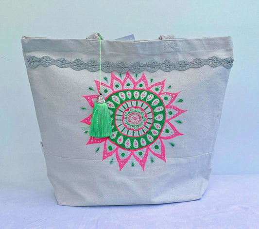 Front view of canvas tote bag, with large hand painted green and pink mandala, silver braid at top, green tassel.