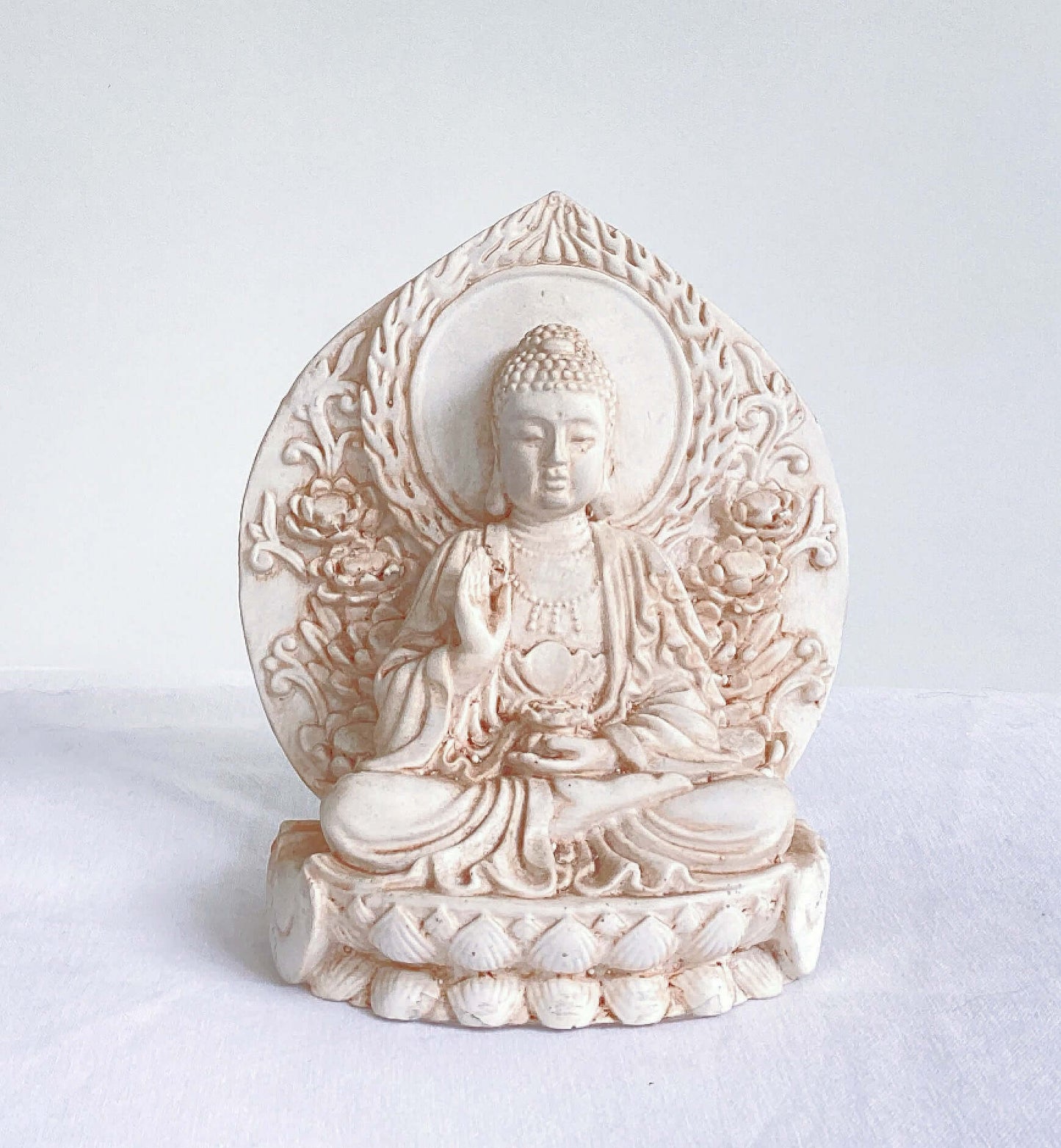 Distant view of buddha, ornate patterns on his robes and pedestal, leaning against a halo surrounding the entire statue.