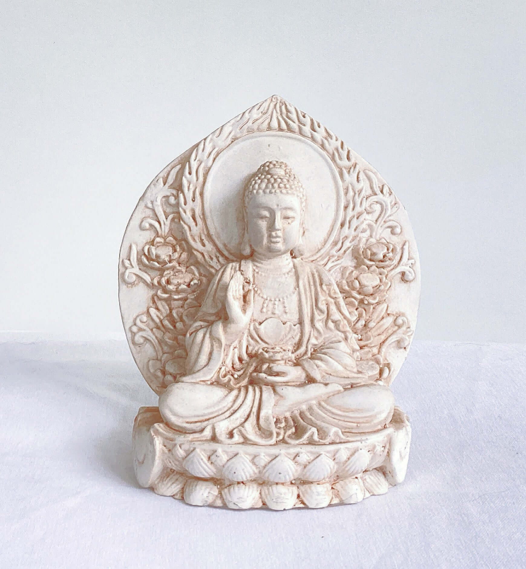 Distant view of buddha, ornate patterns on his robes and pedestal, leaning against a halo surrounding the entire statue.