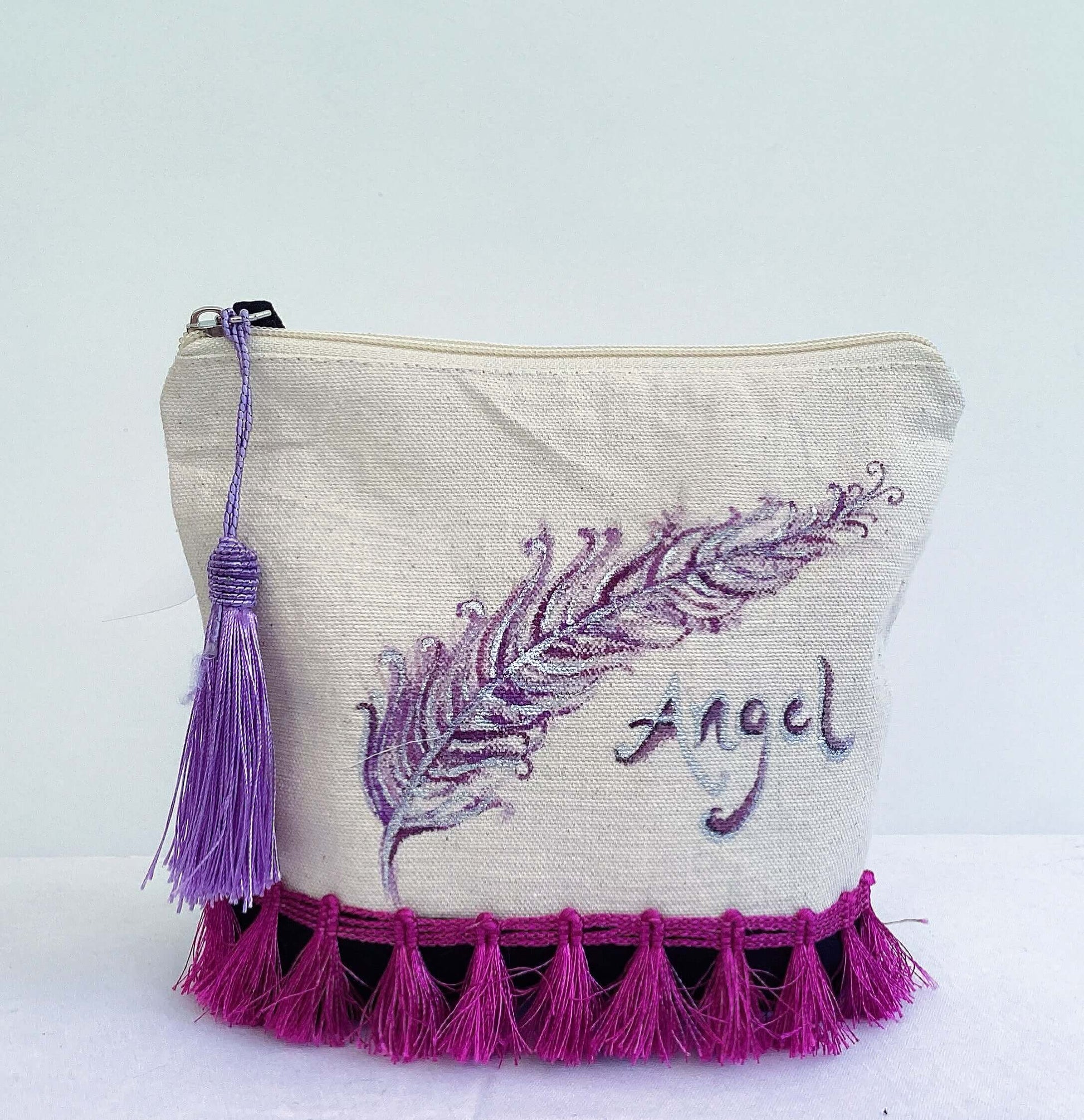 Front of canvas pouch, black canvas base, with hand painted feather, magenta trim at the base, lavender tassel and zip.