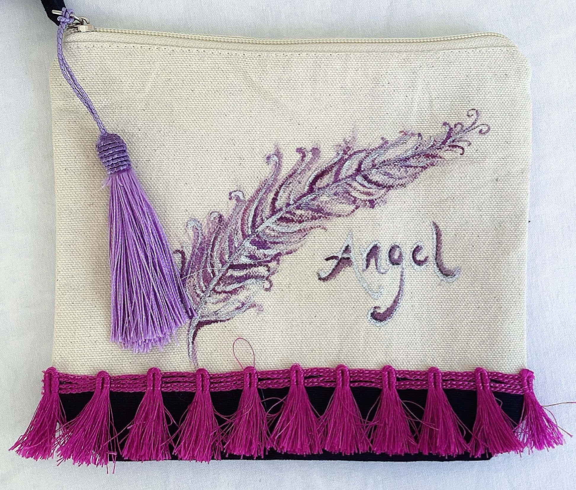 Front of canvas pouch, black canvas base, with hand painted feather, magenta trim at the base, lavender tassel and zip.