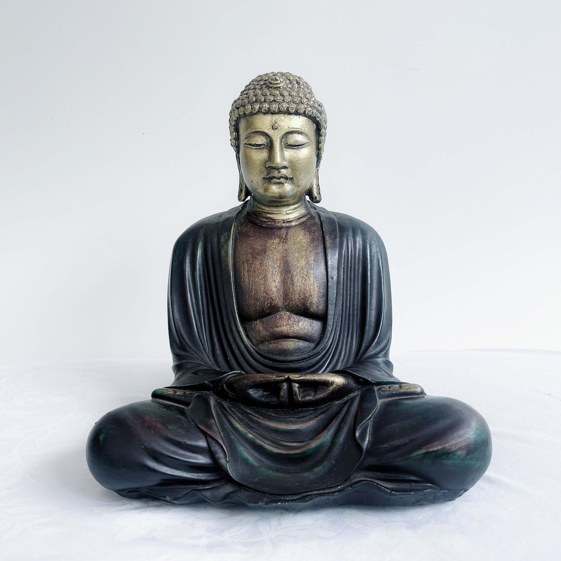Front view of gold and ebony buddha in the meditation position, overall surface is smooth, the robes do not cover the chest area.