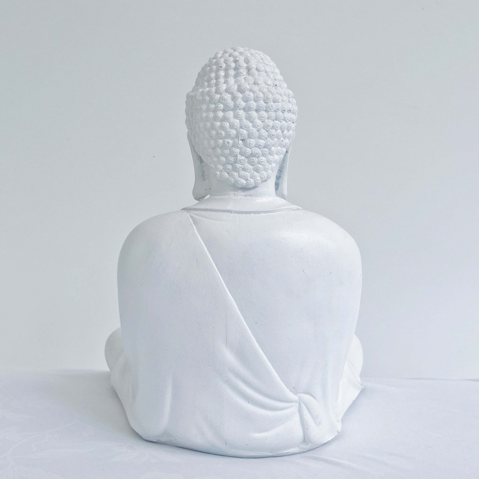 Back view of white buddha in the meditation position, overall surface is smooth.