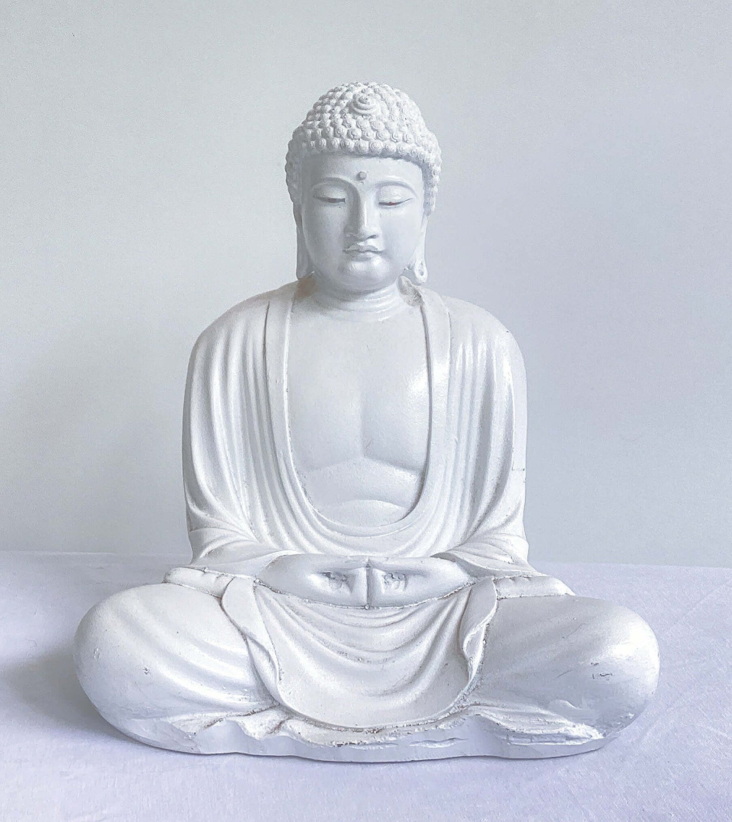 Front view of white buddha in the meditation position, overall surface is smooth, the robes do not cover the chest area.