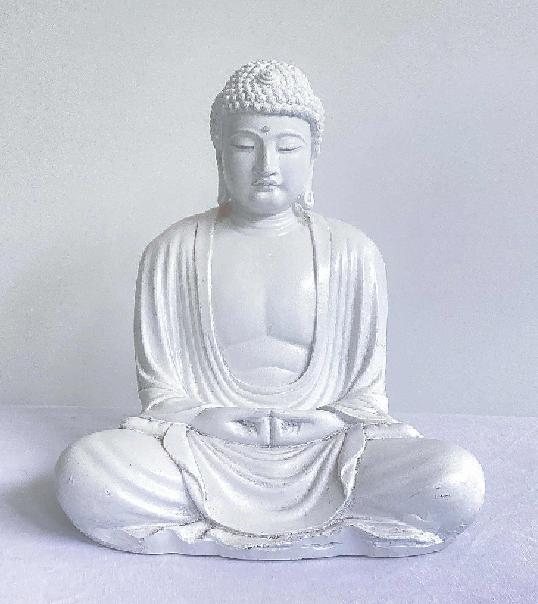 Front view of white buddha in the meditation position, overall surface is smooth, the robes do not cover the chest area.