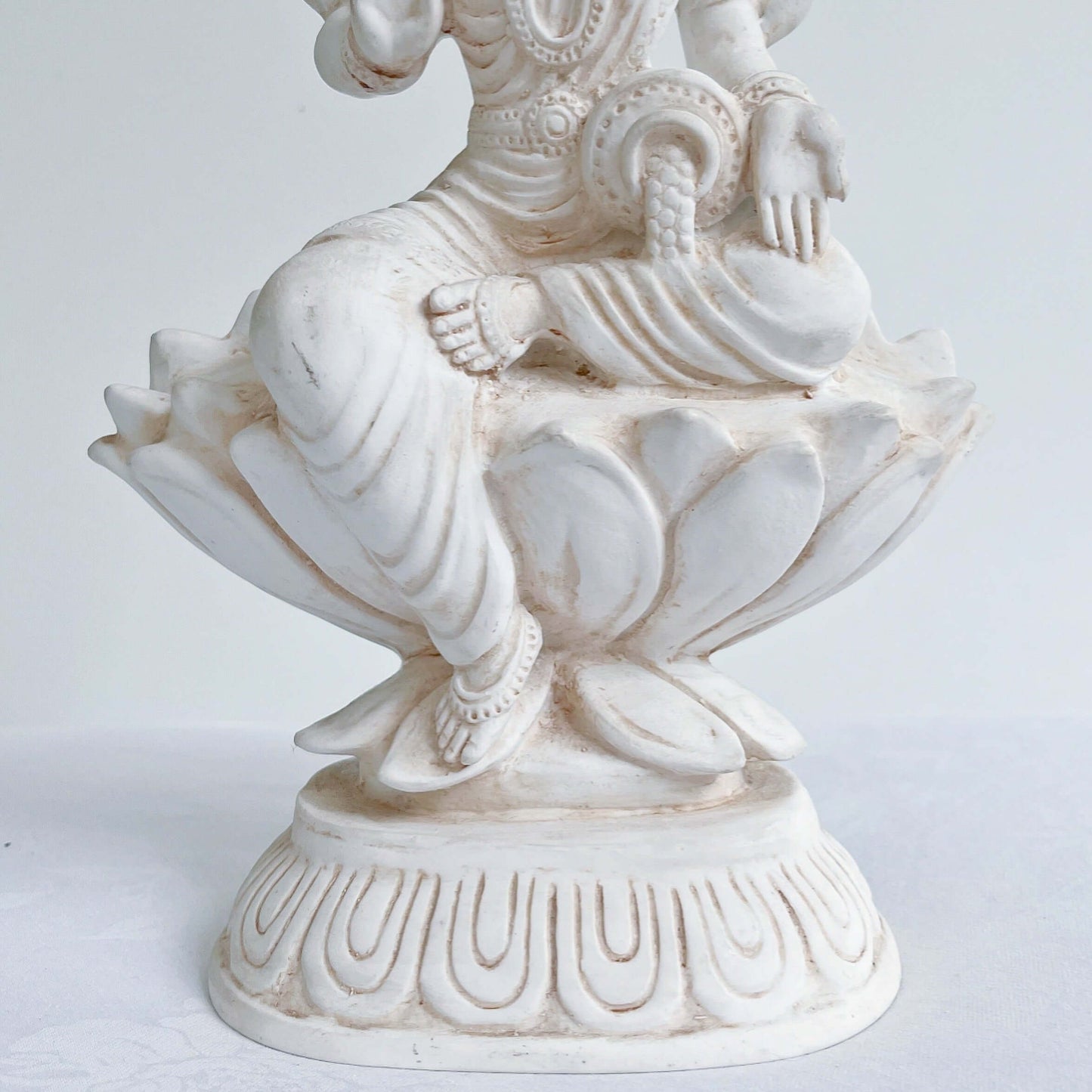 Front bottom half, detail view of Lakshmi, natural off white color, resting on lotus flower and pedestal.