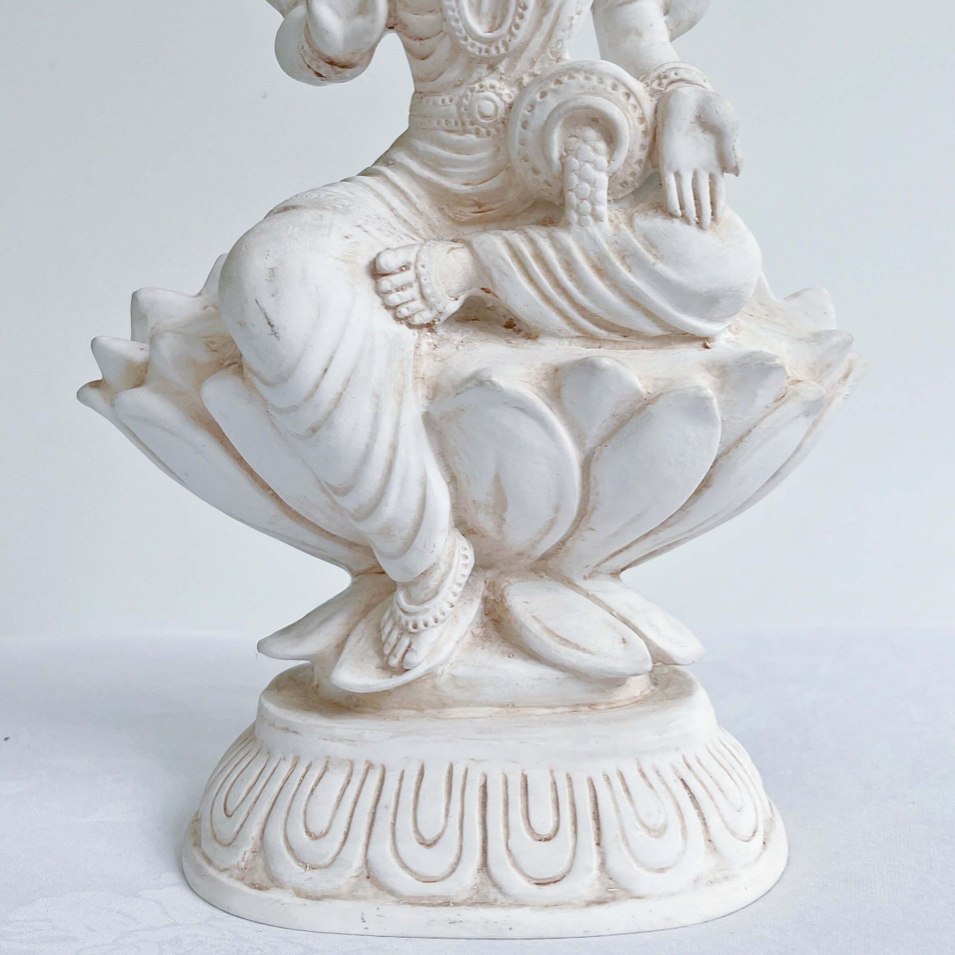 Front bottom half, detail view of Lakshmi, natural off white color, resting on lotus flower and pedestal.