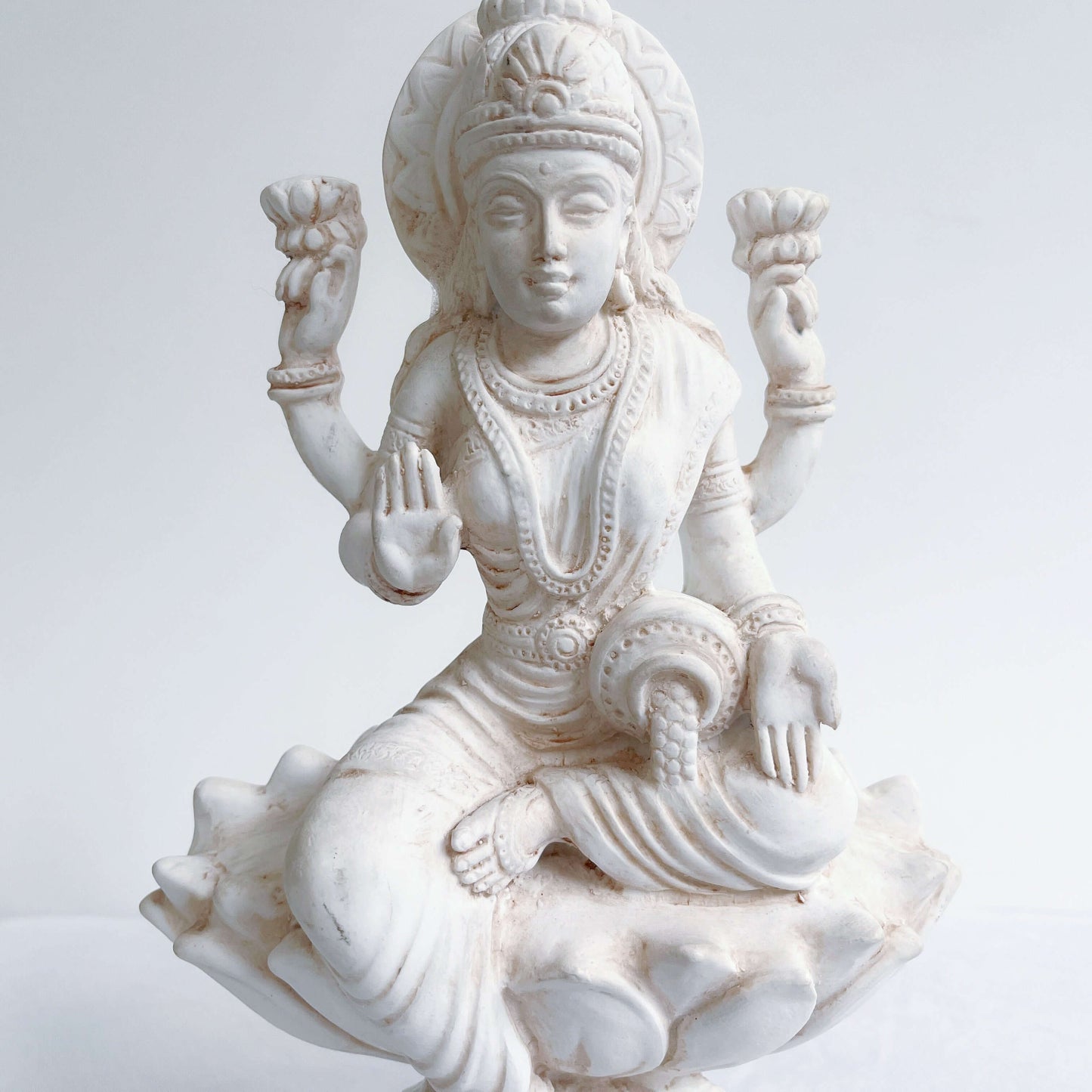 Front detail view of Lakshmi, natural off white color, resting on lotus flower and pedestal.