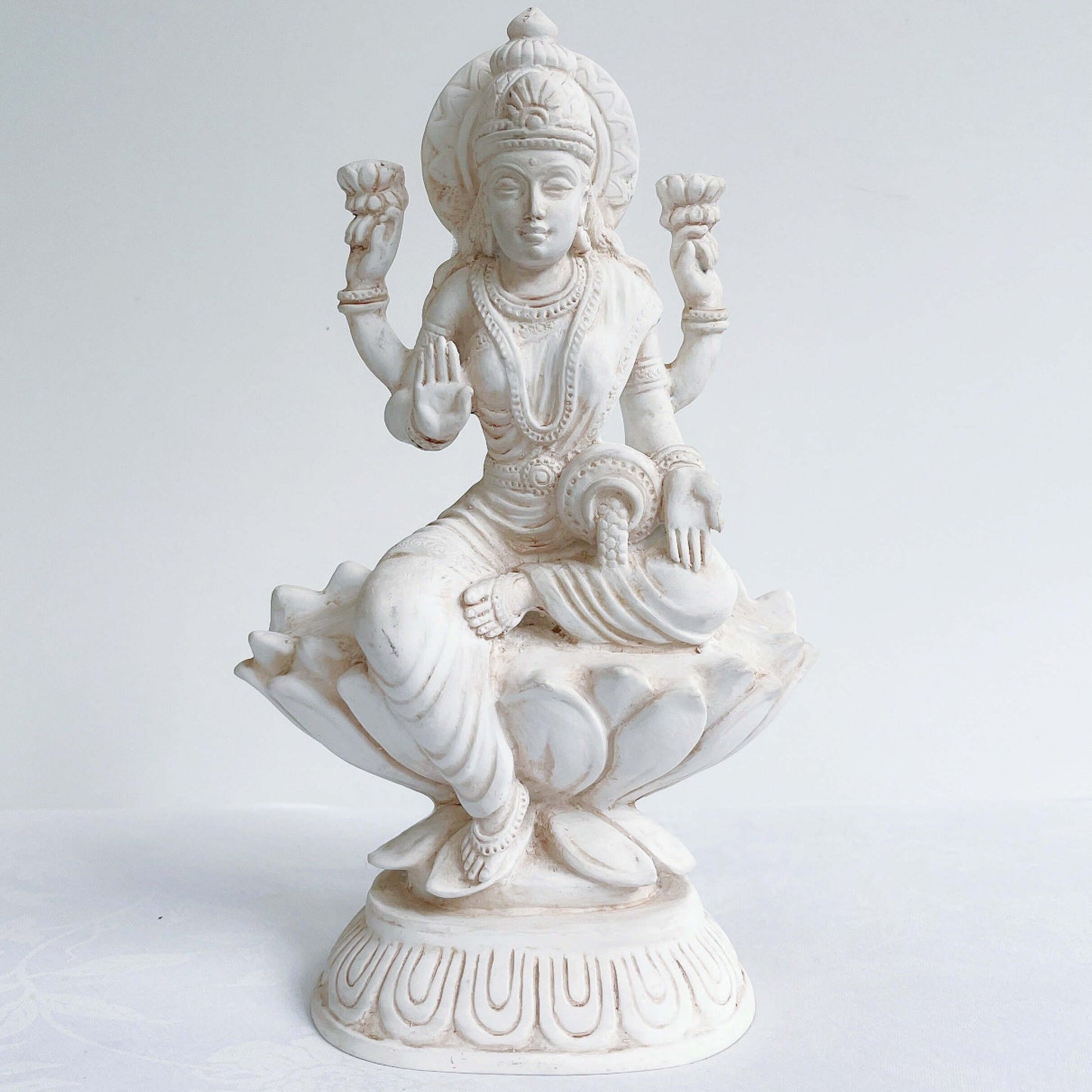 Front view of Lakshmi, natural off white color, resting on lotus flower and pedestal.