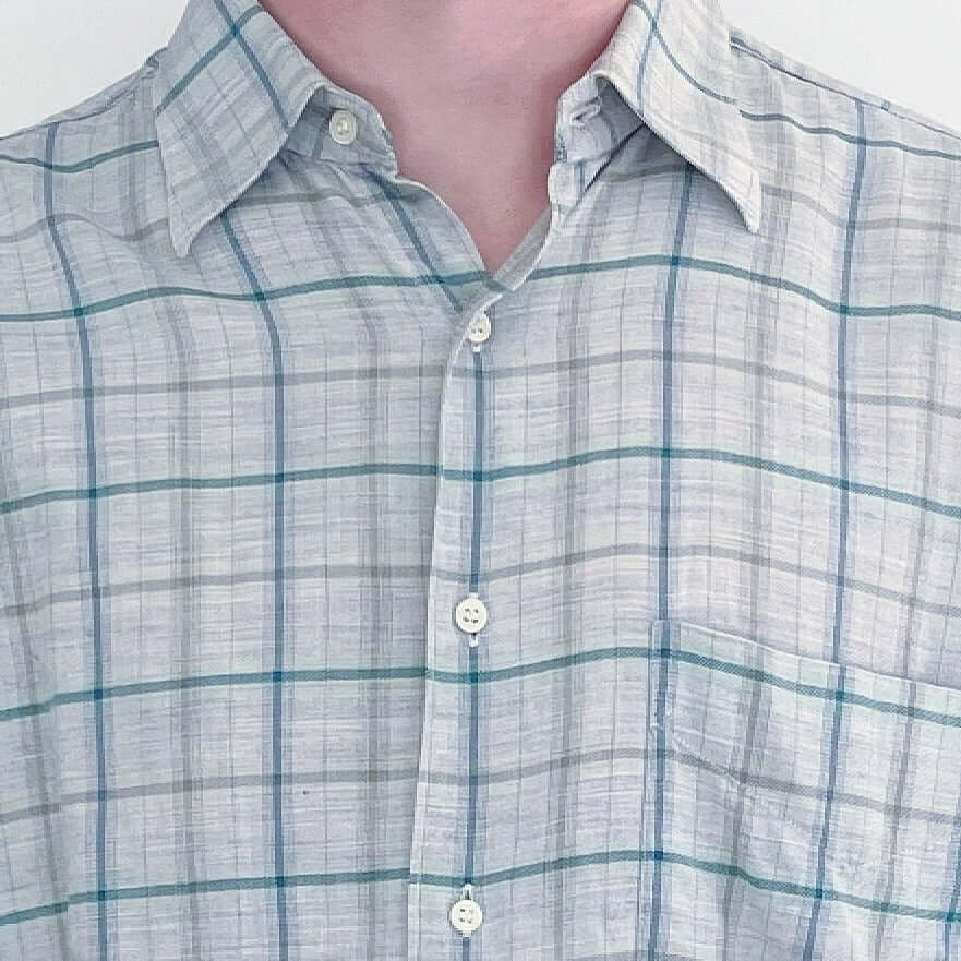 Front detail of the shirt, classic button down style, soft plaid light grey, with a thin teal green and darker gray stripe.