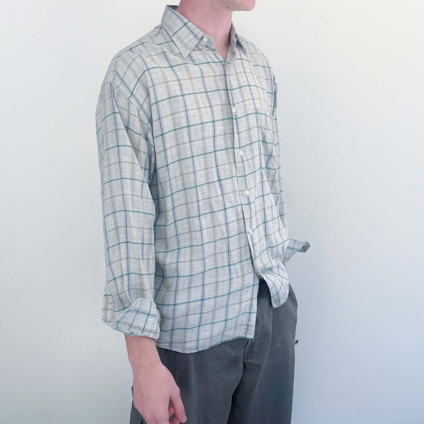 Side view of the shirt, classic button down style, soft plaid light grey, with a thin teal green and darker gray stripe.