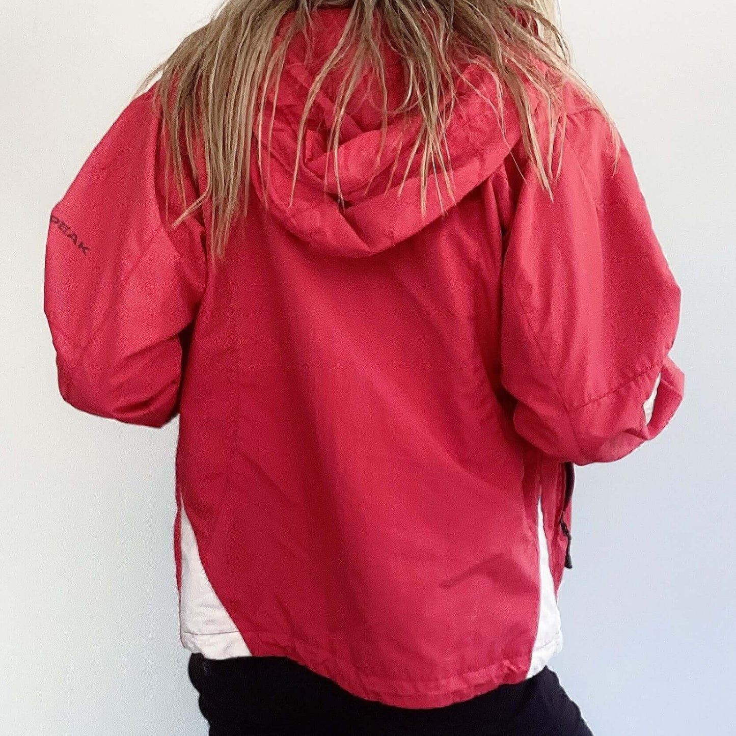 Back view of hip length, red zipper jacket, with hood and some black and white trim on the edges.