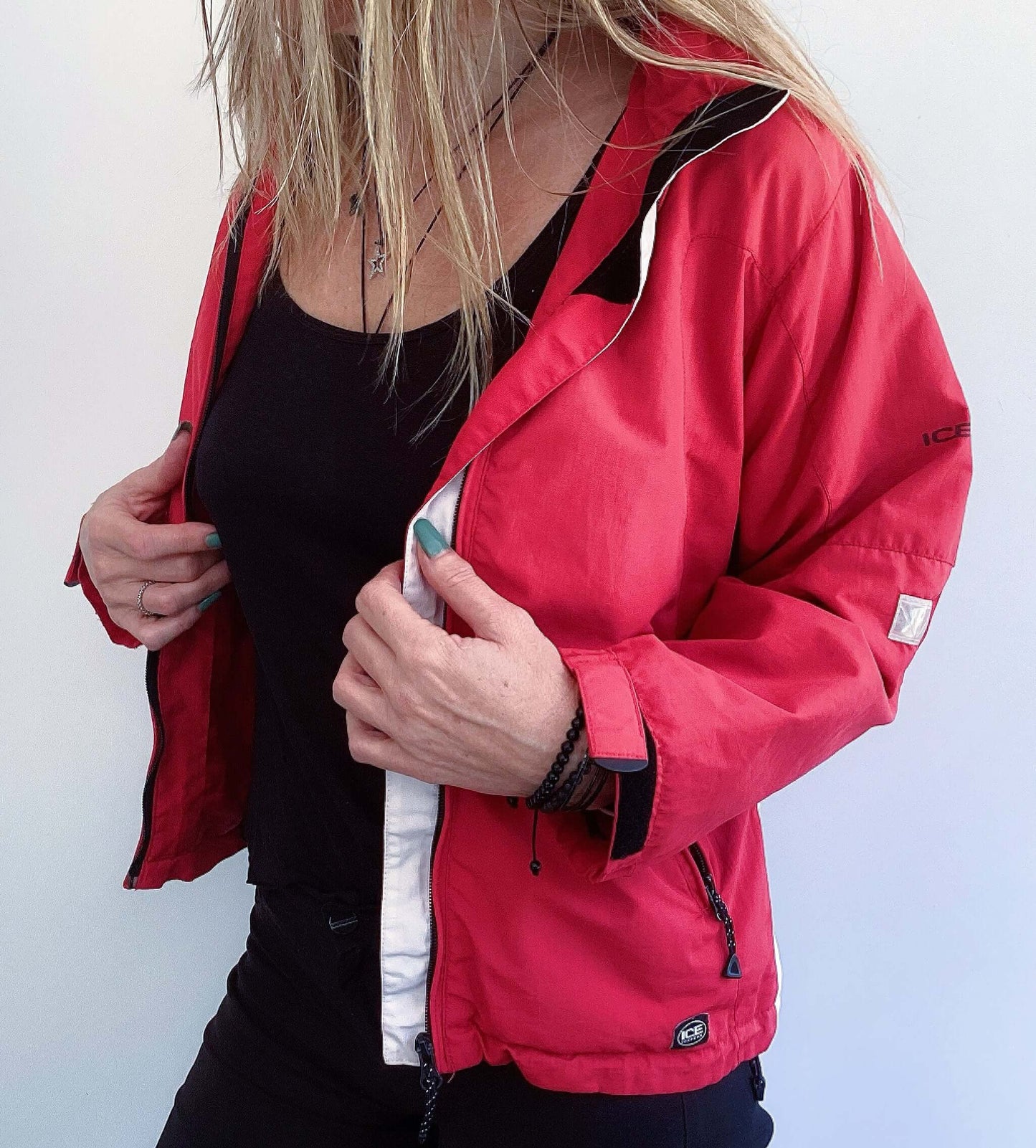 Side view of hip length, red zipper jacket, with hood and some black and white trim on the edges.