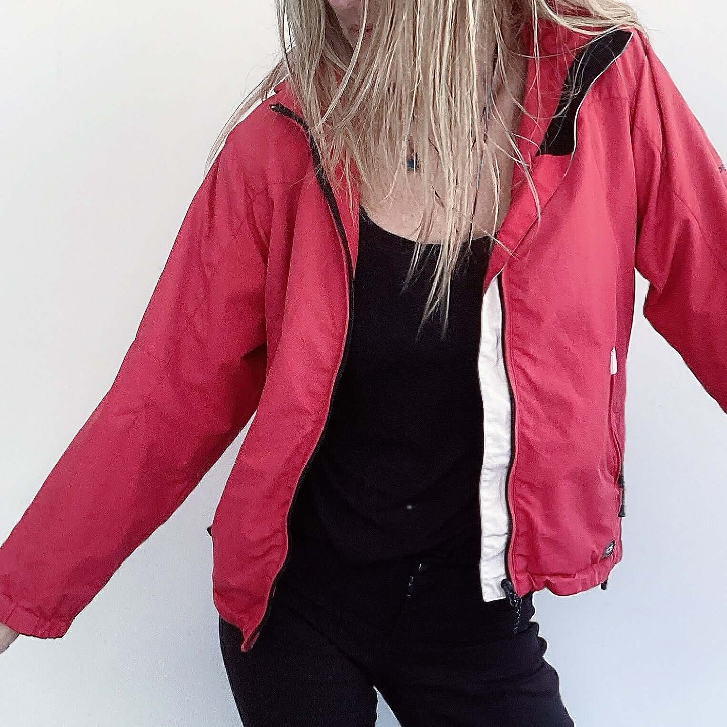 Front view of hip length red zipper jacket, with hood and some black and white trim on the edges.