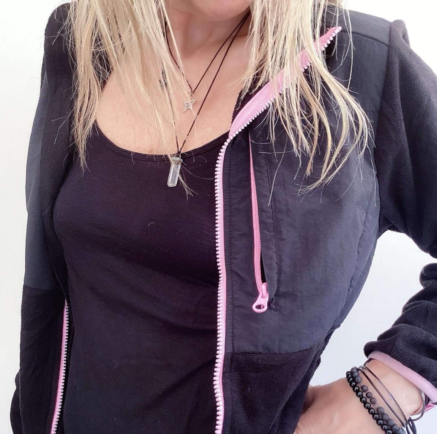 Detail view of black zipper jacket, pink trim on the edges, with one vertical breast pocket and side pockets, hip length.