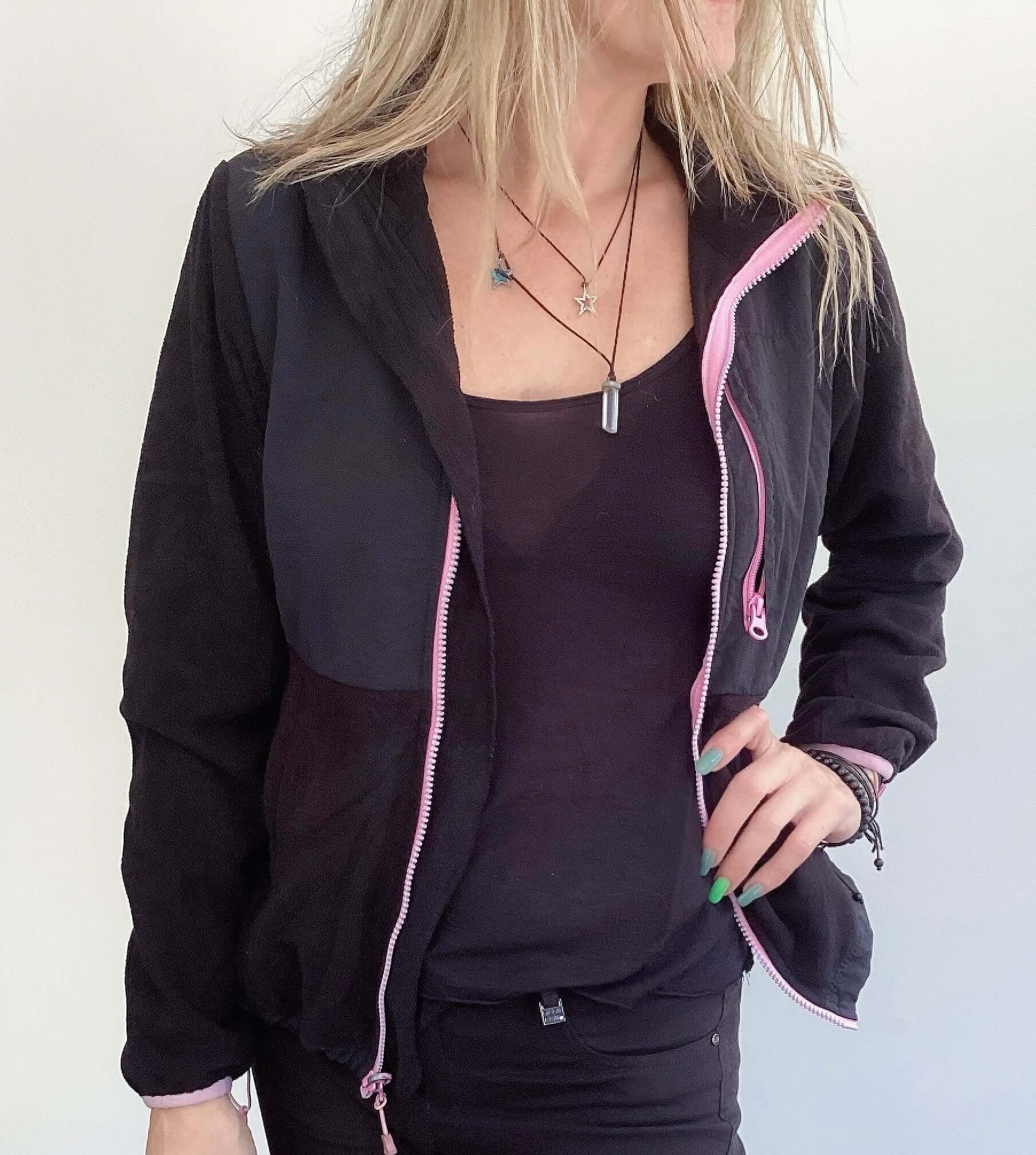 Side view of black zipper jacket, pink trim on the edges, with pockets, hip length.