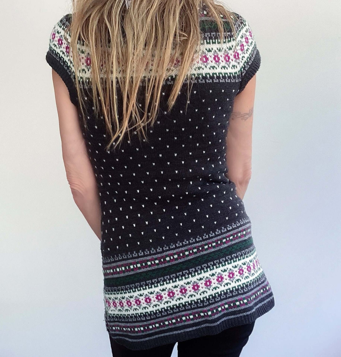 Back view of dark grey purl stitch cardigan, white flecks, and white, pink, green detailing at edges, upper thigh length.