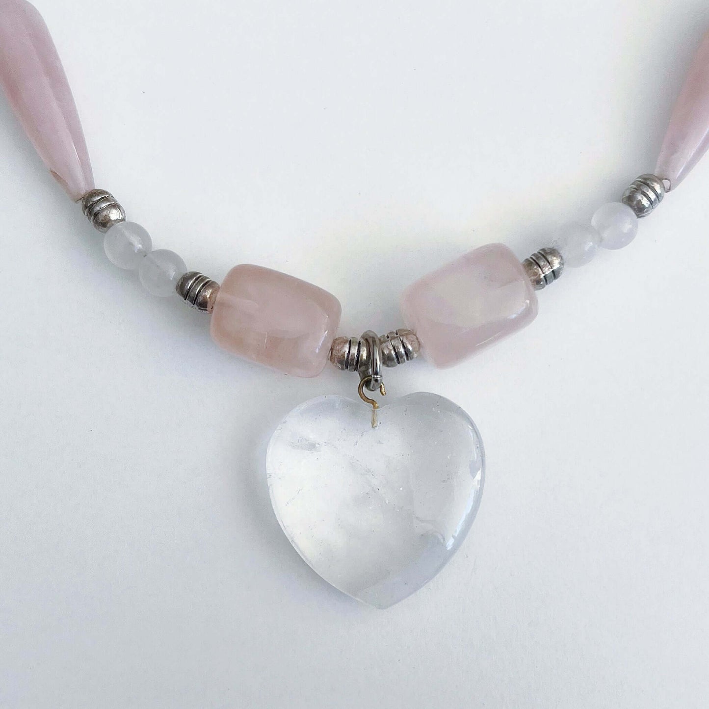 Detail view of the Clear Quartz heart pendant, with assorted sized Rose Quartz beads on either side.