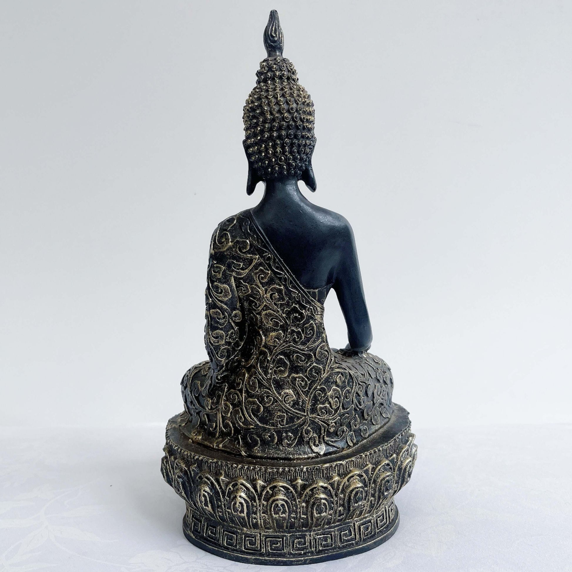 Back view of buddha in lotus position, black and gold paint wash, ornate robes and pedestal, ushnisha on head.