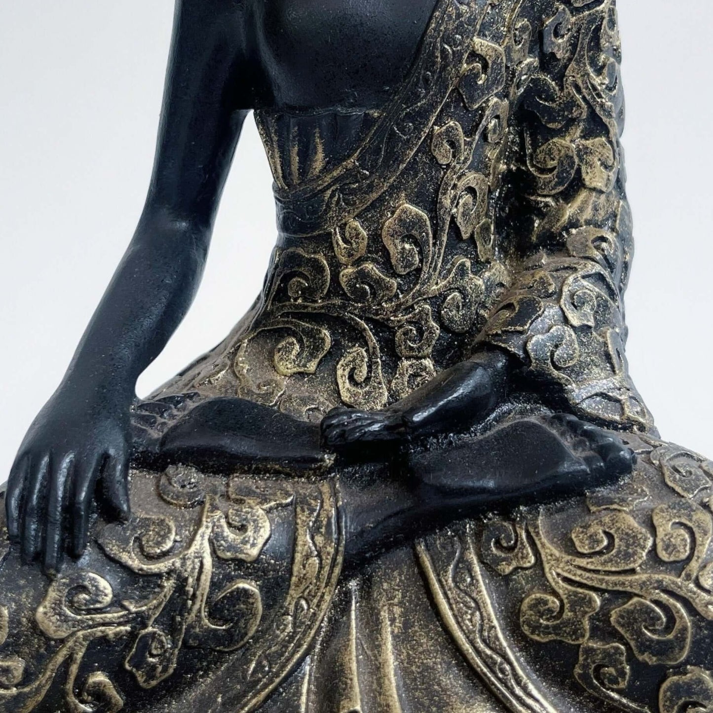 Front detail view of buddha in lotus position, black and gold paint wash, ornate robes and pedestal.