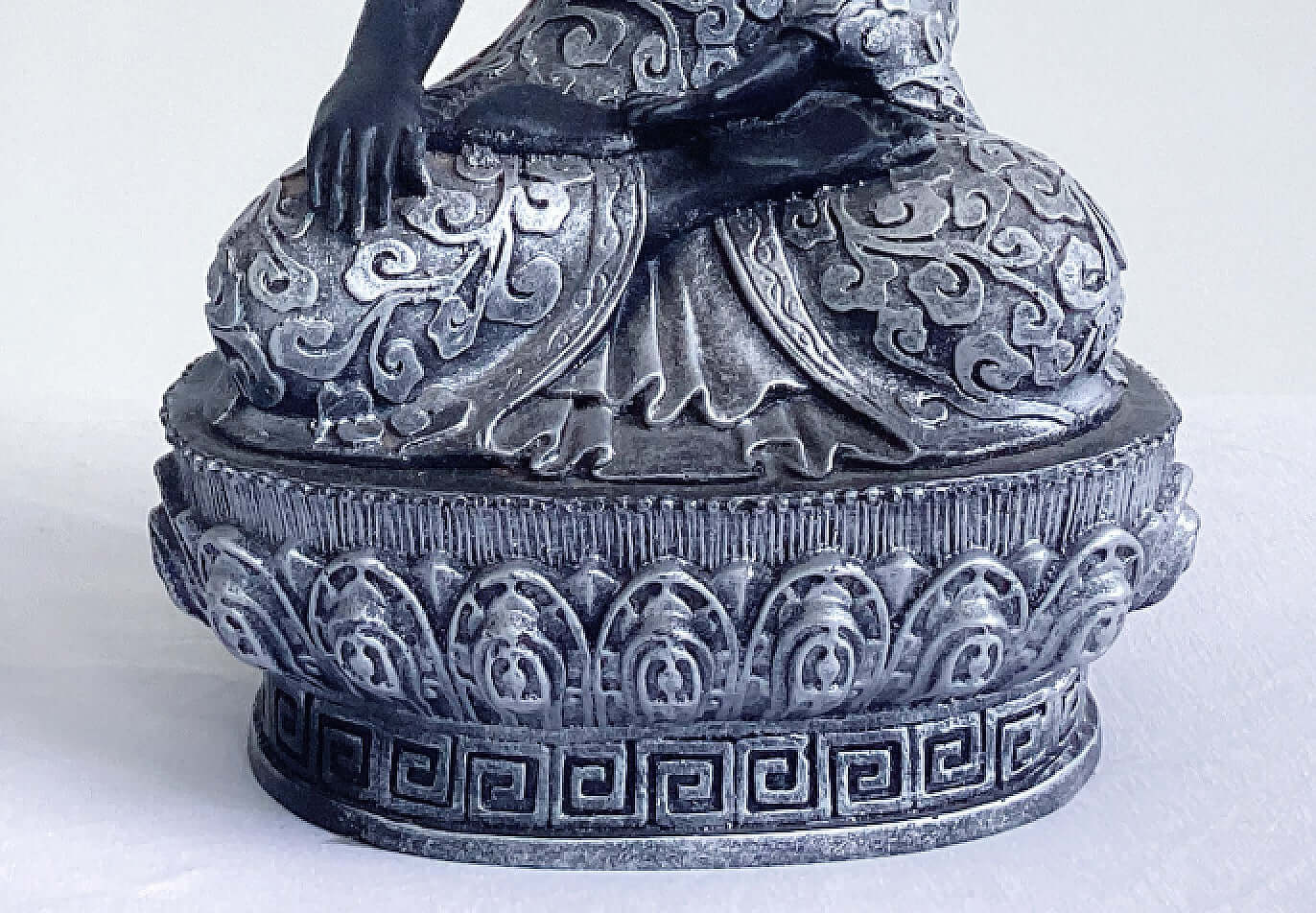 Front detail view of buddha in lotus position, black and silver paint wash, ornate robes and pedestal.