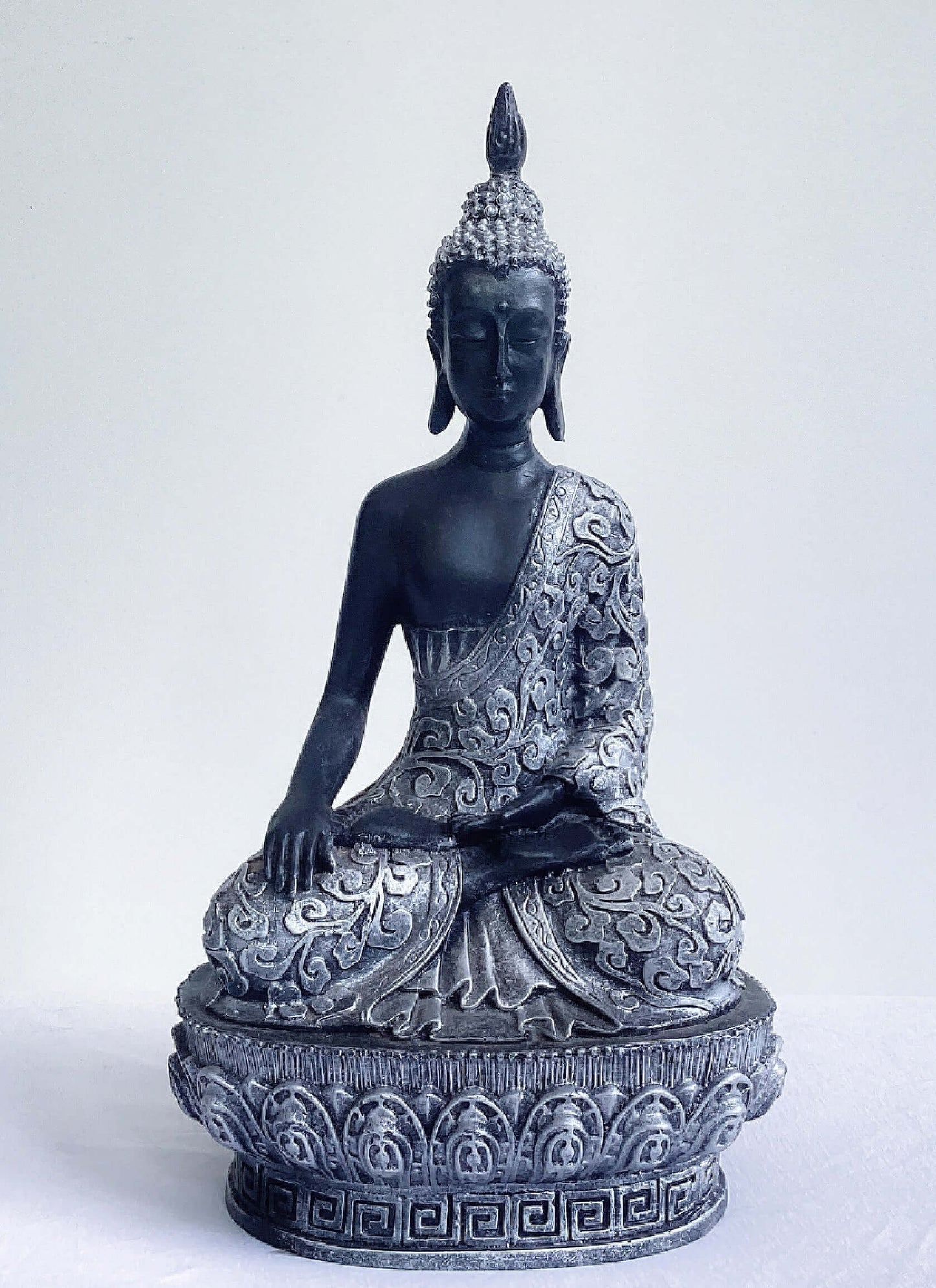 Front view of buddha in lotus position, black and silver paint wash, ornate robes and pedestal, ushnisha on head.