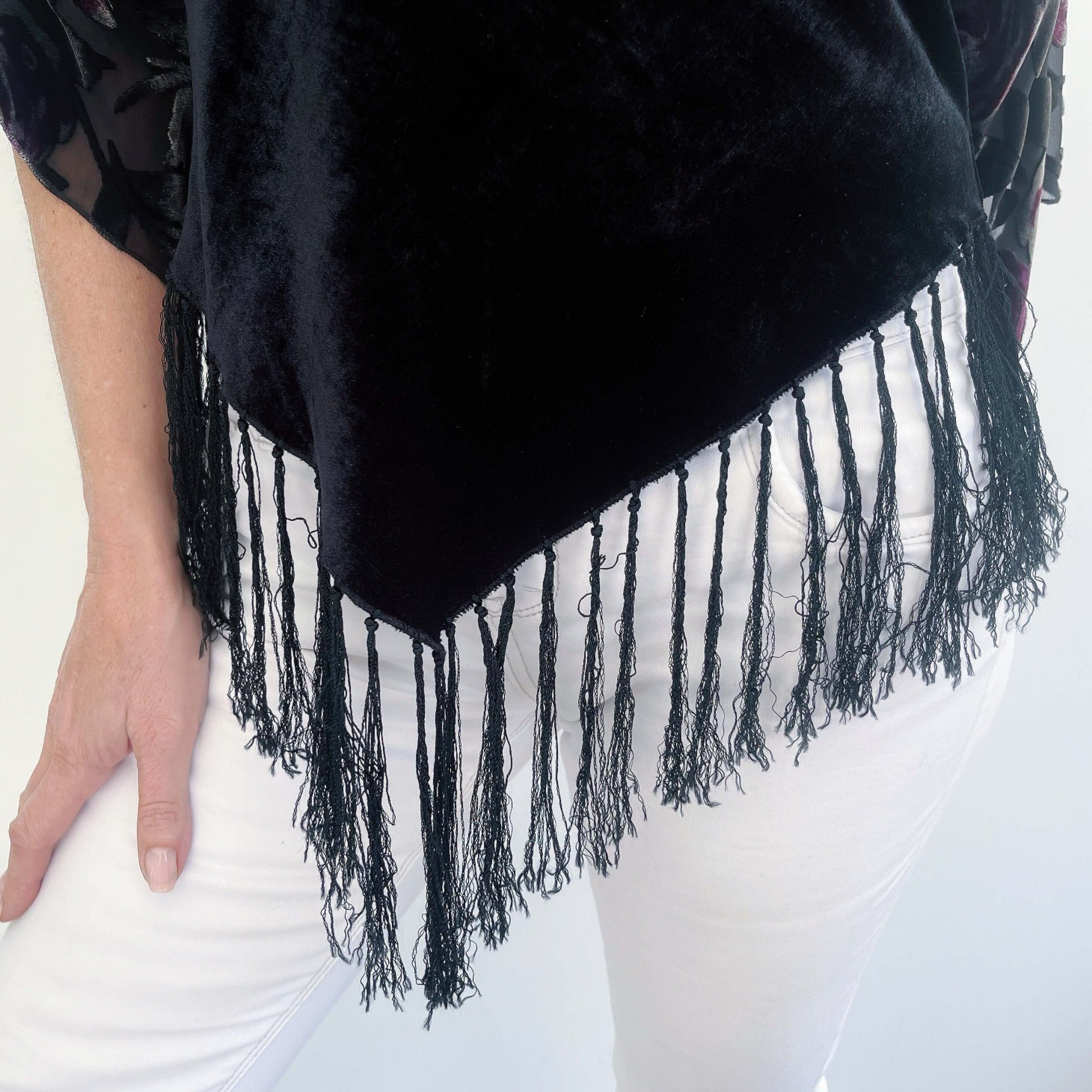 Detail view of the v shaped hem of the black velvet torso section dipping to a V, at center front and back with the fringing.